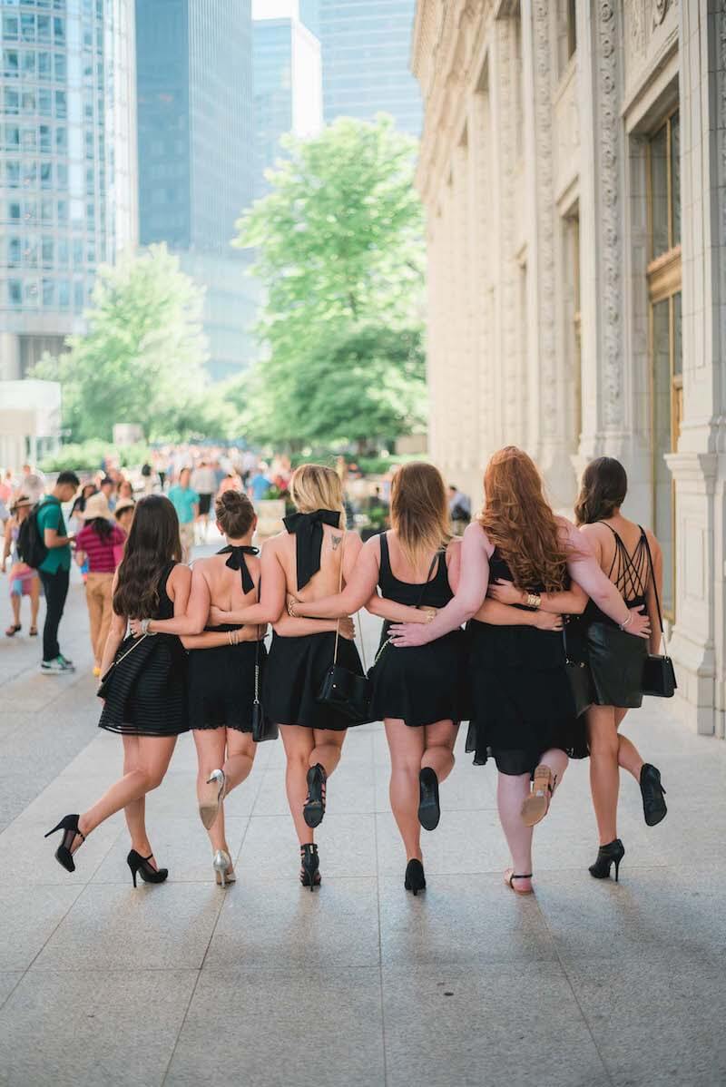 Six female friends on a bachelorette trip walking together with their arms around each other's waists in Chicago, USA