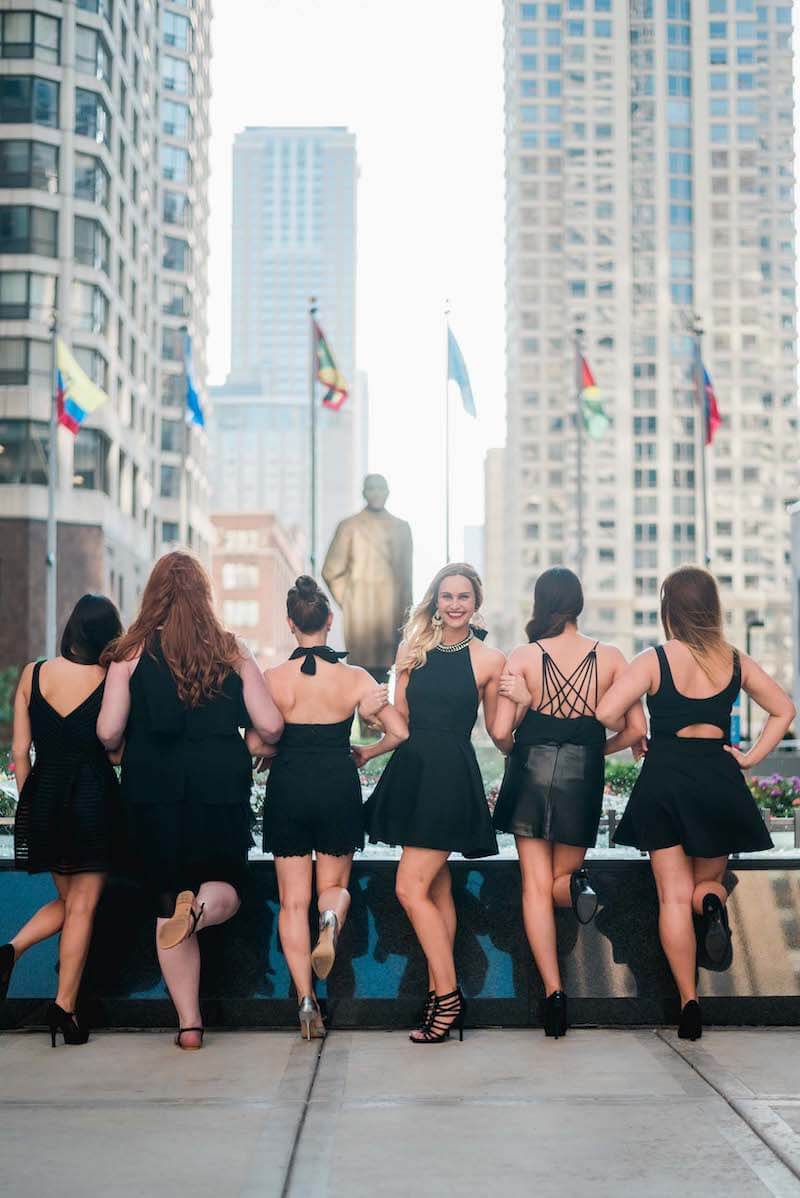 Six female friends on a bachelorette trip standing in front of a fountain with 5 woman facing away and 1 woman facing the camera in Chicago, USA