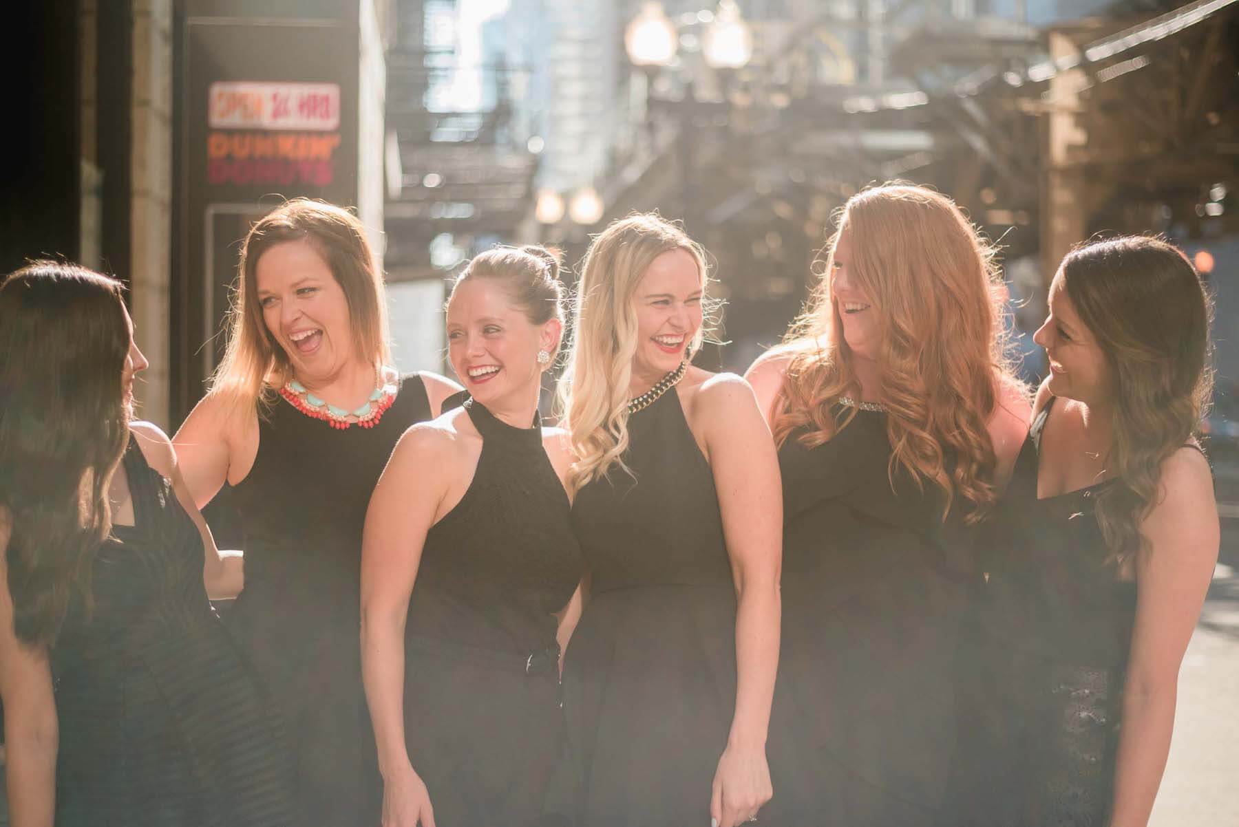 Six female friends standing together laughing with one another on a bachelorette trip in Chicago, USA