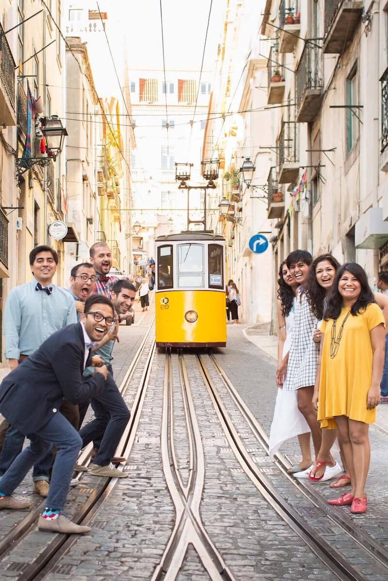 Family of nine smiling and pointing at a yellow trolley in the Bica district of Lisbon, Portugal