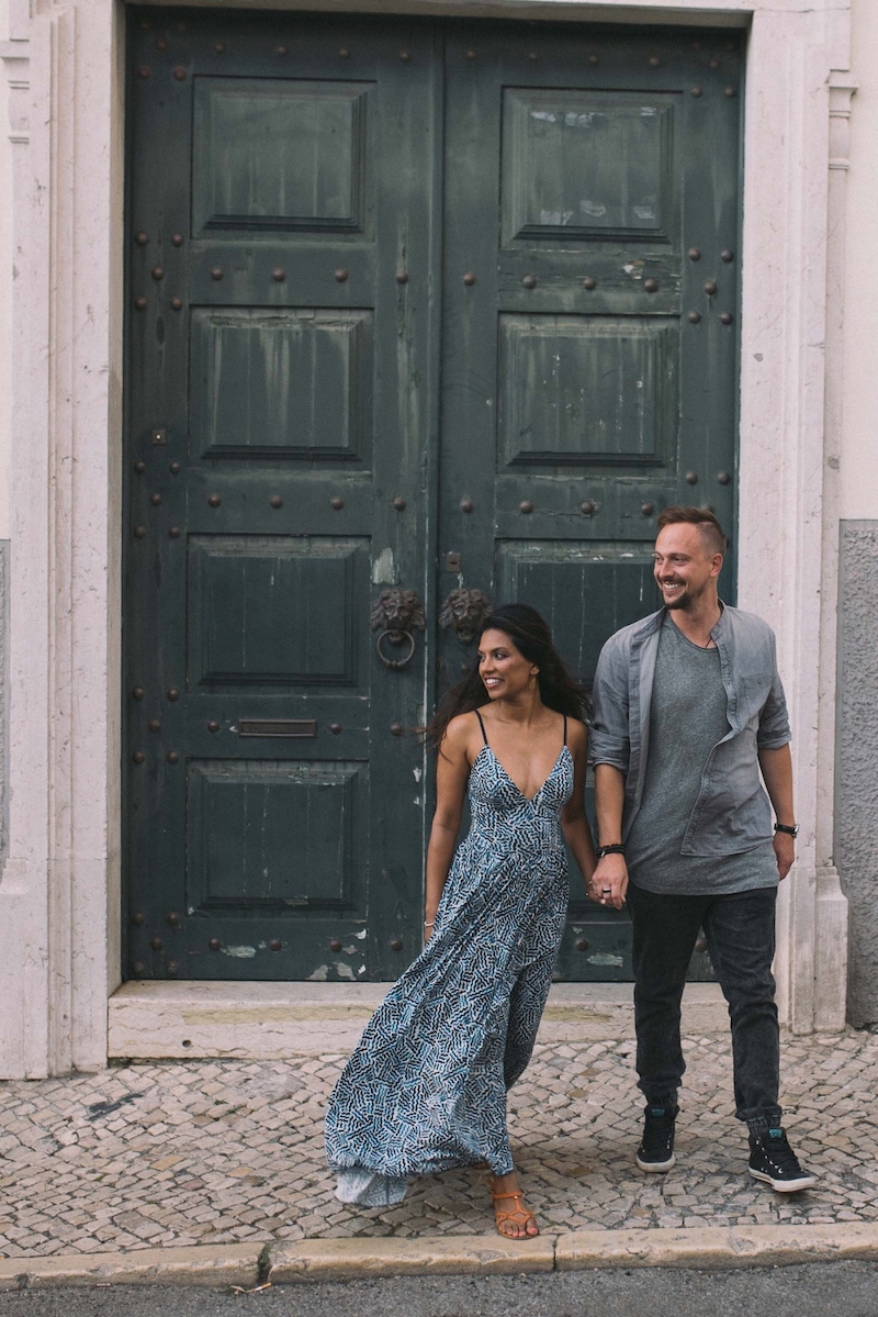 Couple standing in front of large green doorway and holding hands, smiling together in Lisbon, Portugal