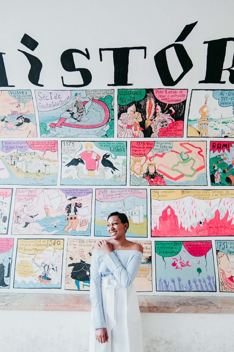Solo female traveller smiling and standing in front of the Lisbon Comic Wall in Lisbon, Portugal