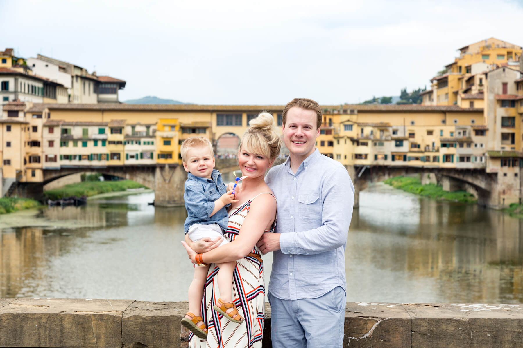Young family with toddler son in front of Ponte Vecchio on family trip in Florence, Italy