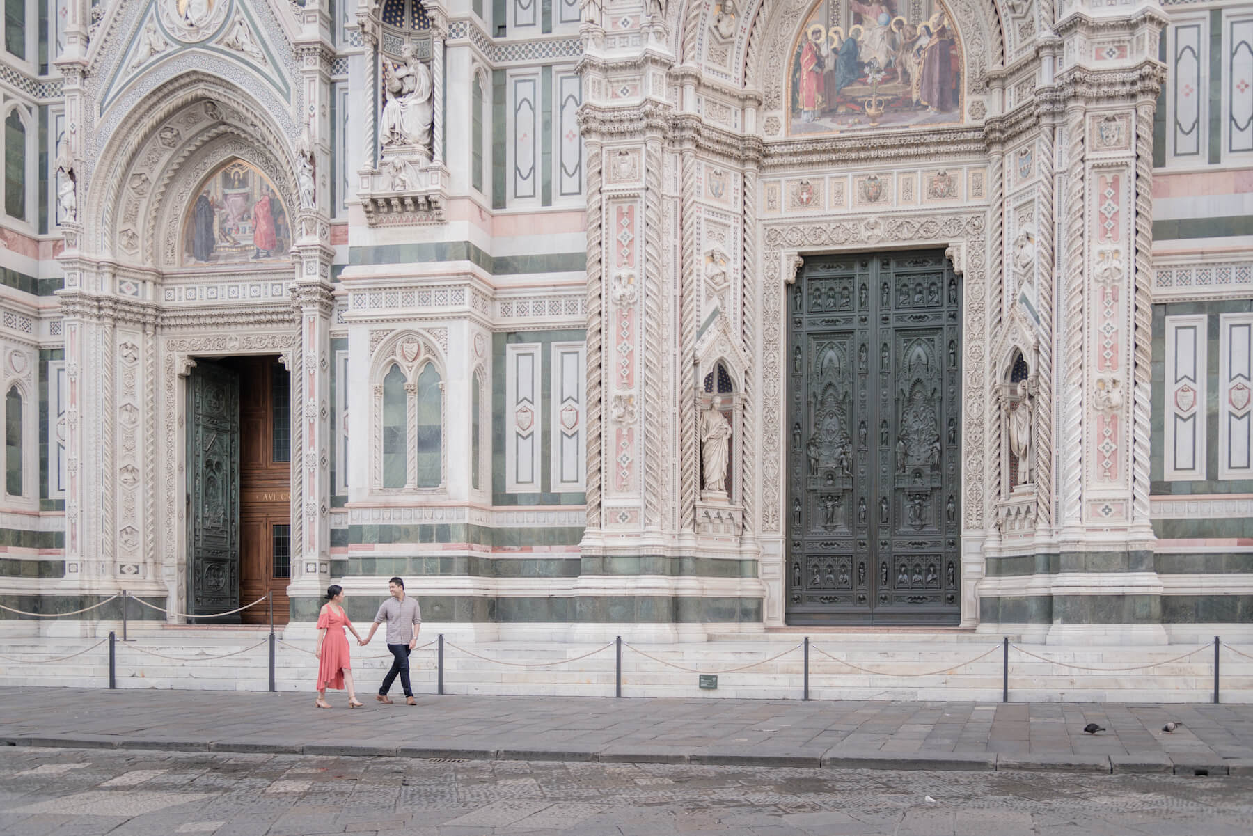 Asian couple holding hands and walking in front of The Duomo on a couples trip in Florence, Italy