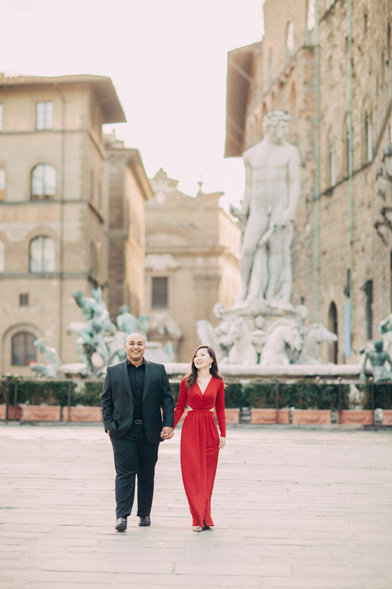 Couple holding hands and walking in front of the fountain of Neptune at Piazza della Signoria in Florence, Italy