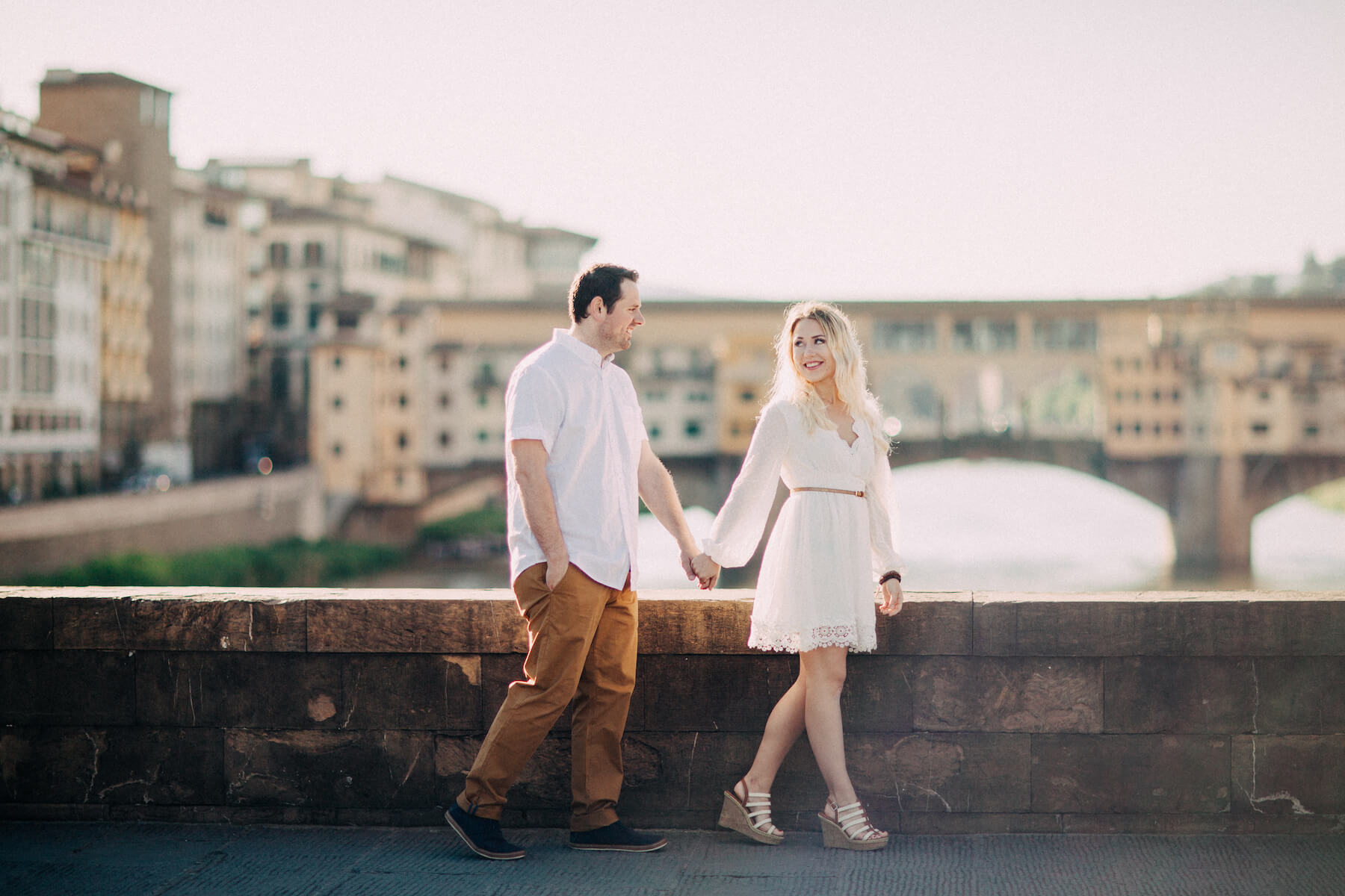 Couple holding hands and walking on bridge in front of Ponte Vecchio in Florence, Italy
