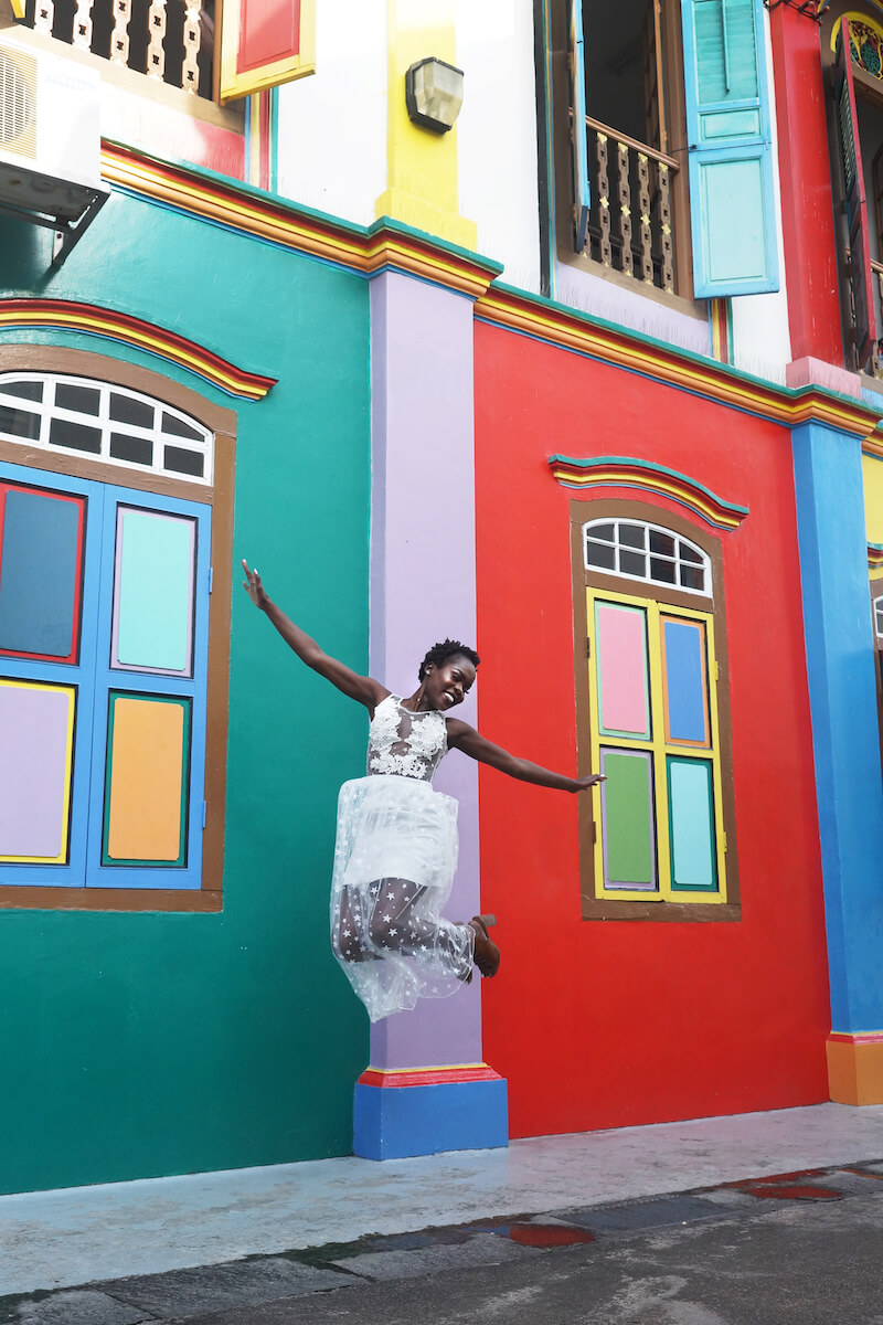 Woman jumping in the air in front of bright coloured building in Singapore