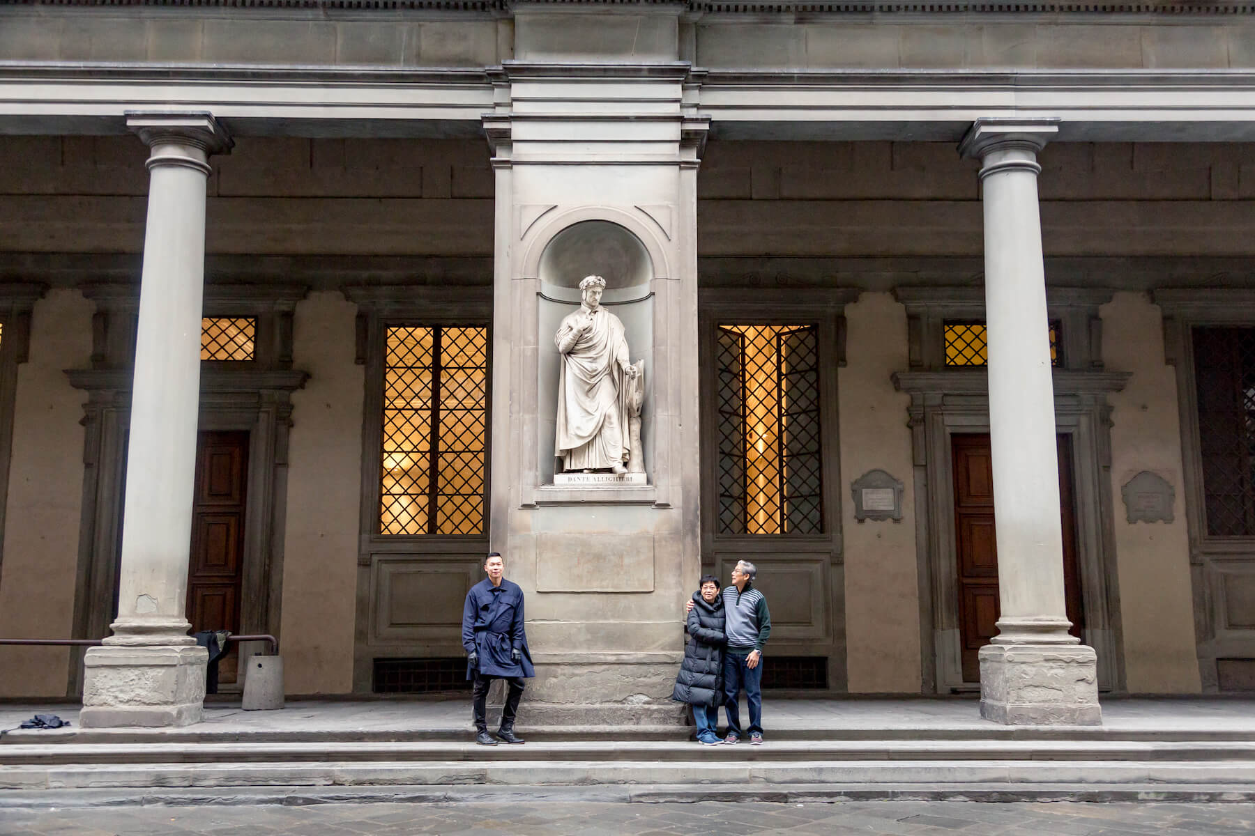 Asian father, mother and adult son standing in front of the statue of poet Dante Alighieri on a family trip together in Florence, Italy