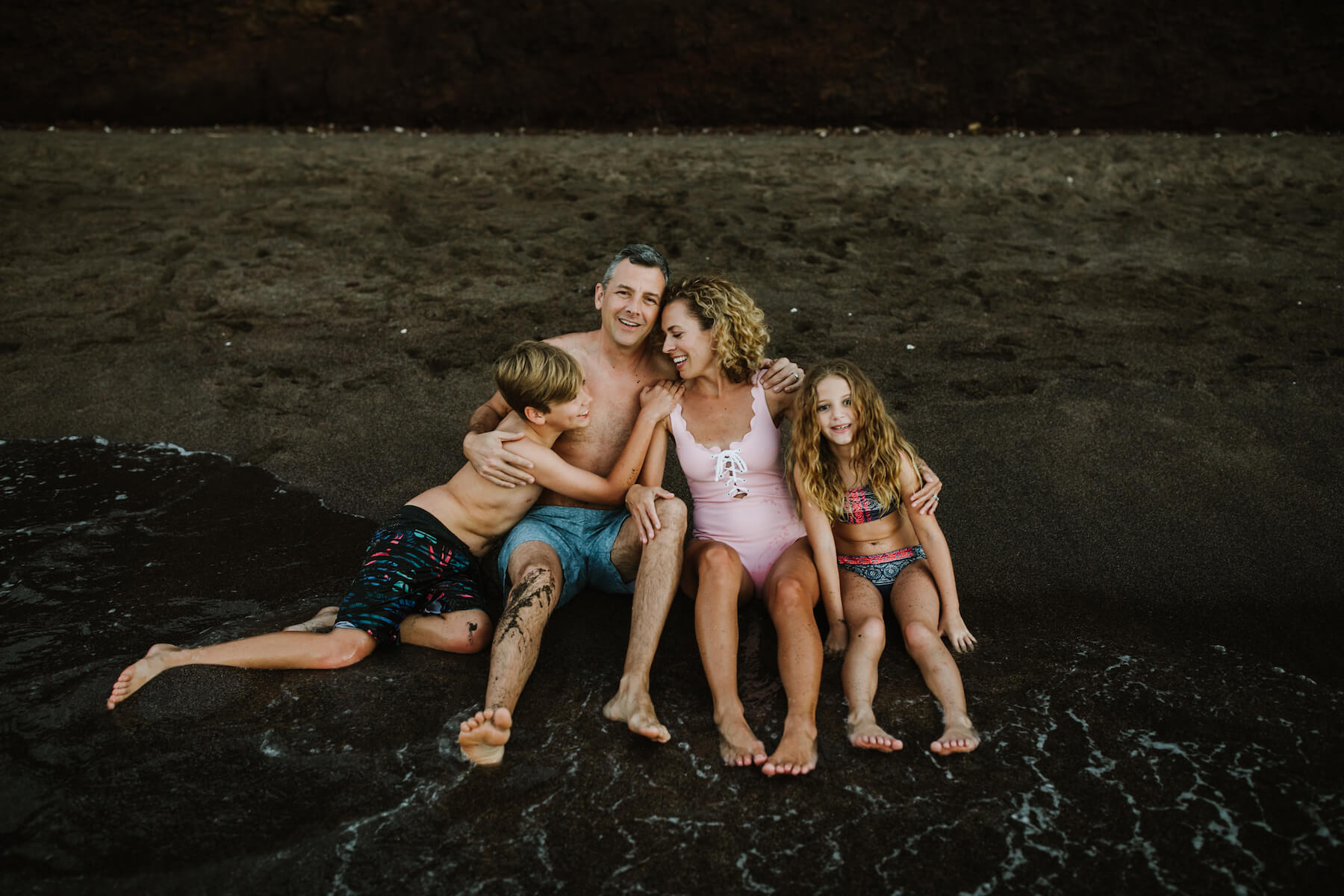 Family of four sitting on a black sand beach in Maui, Hawaii USA