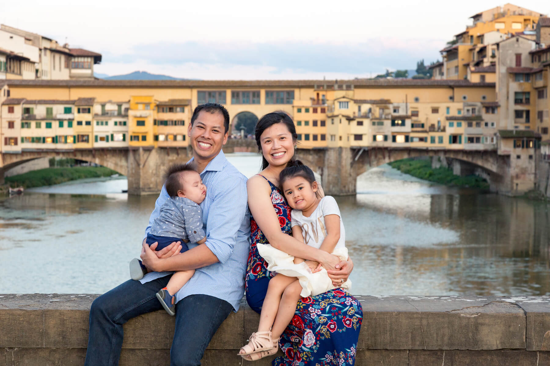 Happy asian family with two children sitting on bridge ledge at Ponte Vecchio in Florence, Italy