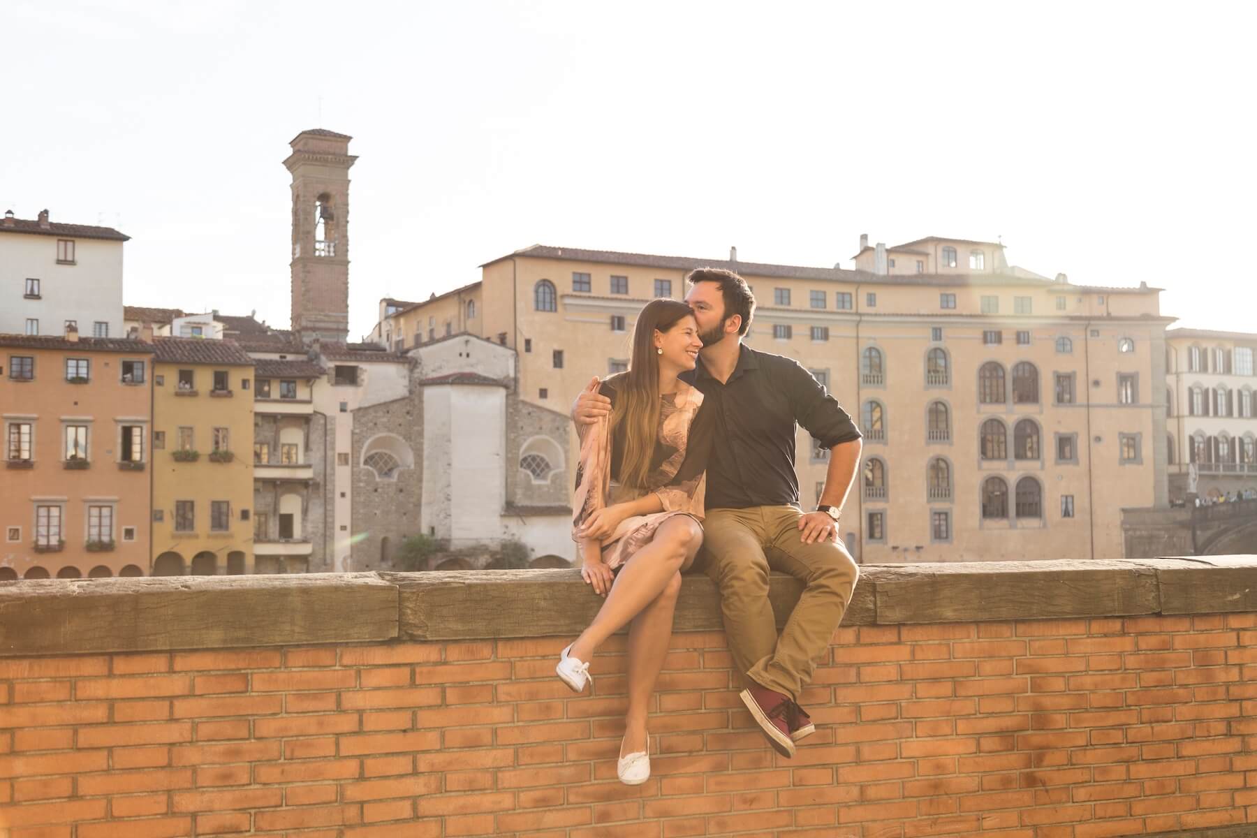 Couple sitting on wall ledge together kissing on couples trip in Florence, Italy