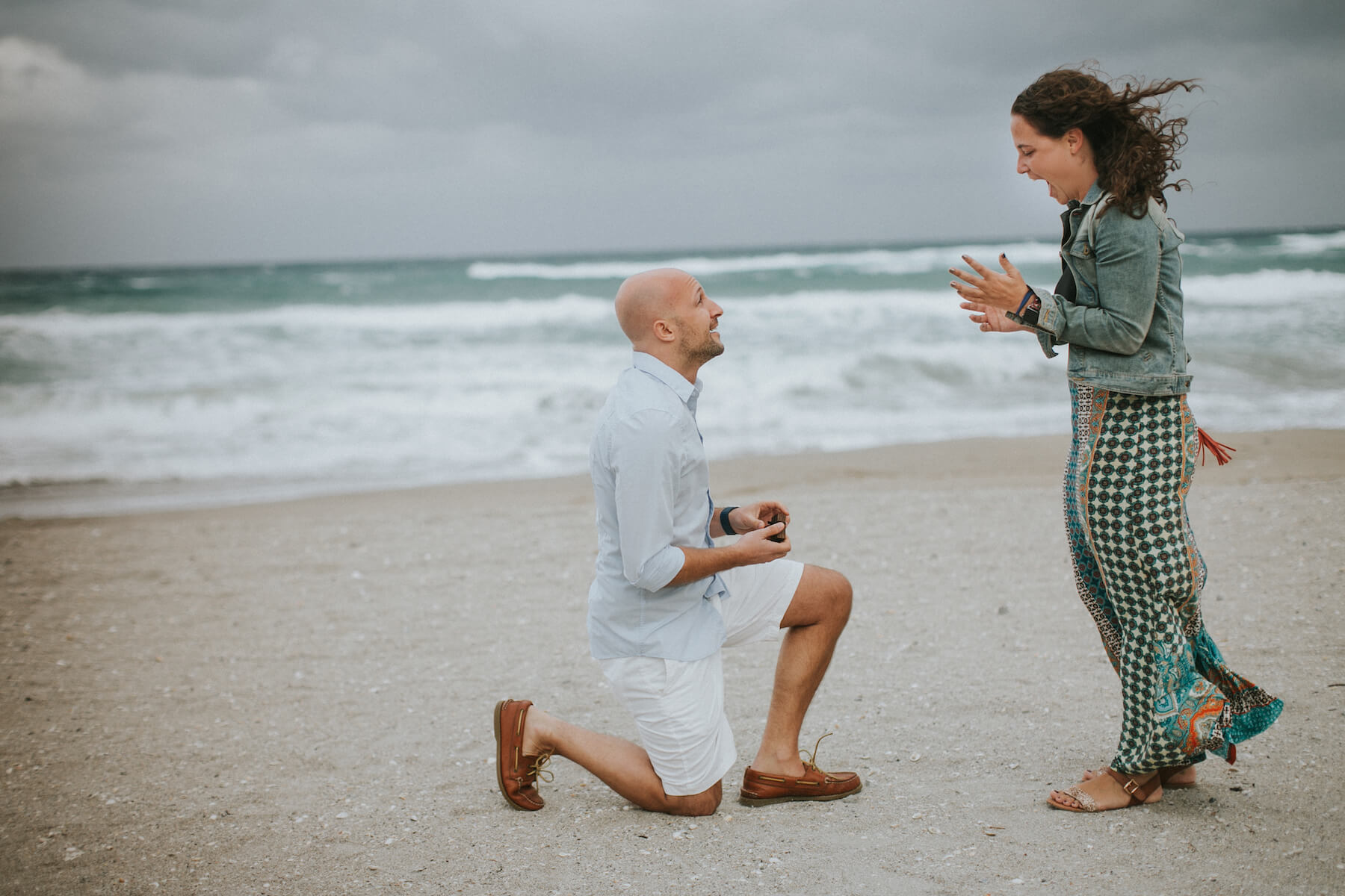 Woman surprised at surprise Flytographer proposal while her partner presents her engagement ring in Miami, Florida USA