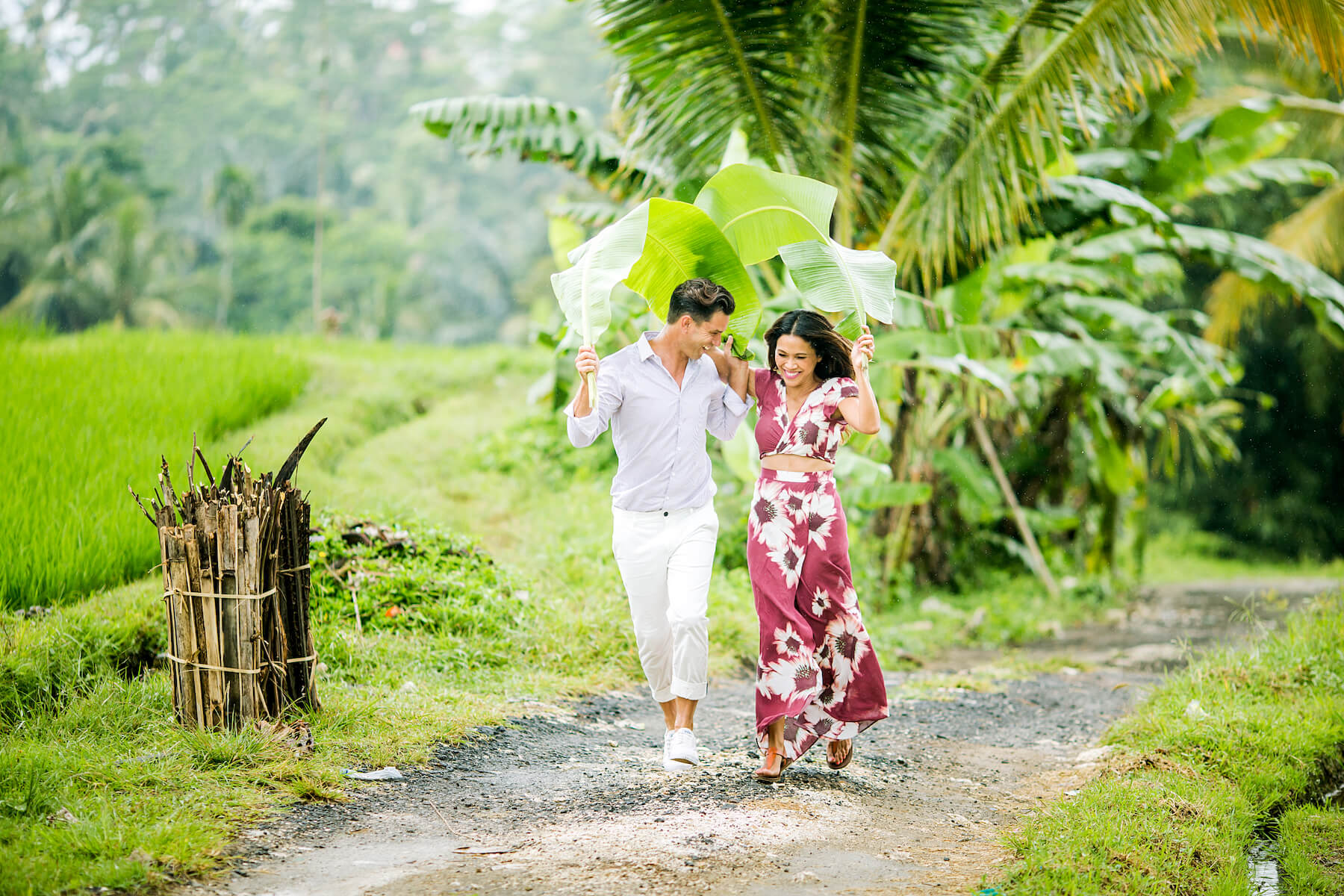 Couple running from the rain together using giant leaves as umbrellas in Bali, Indonesia