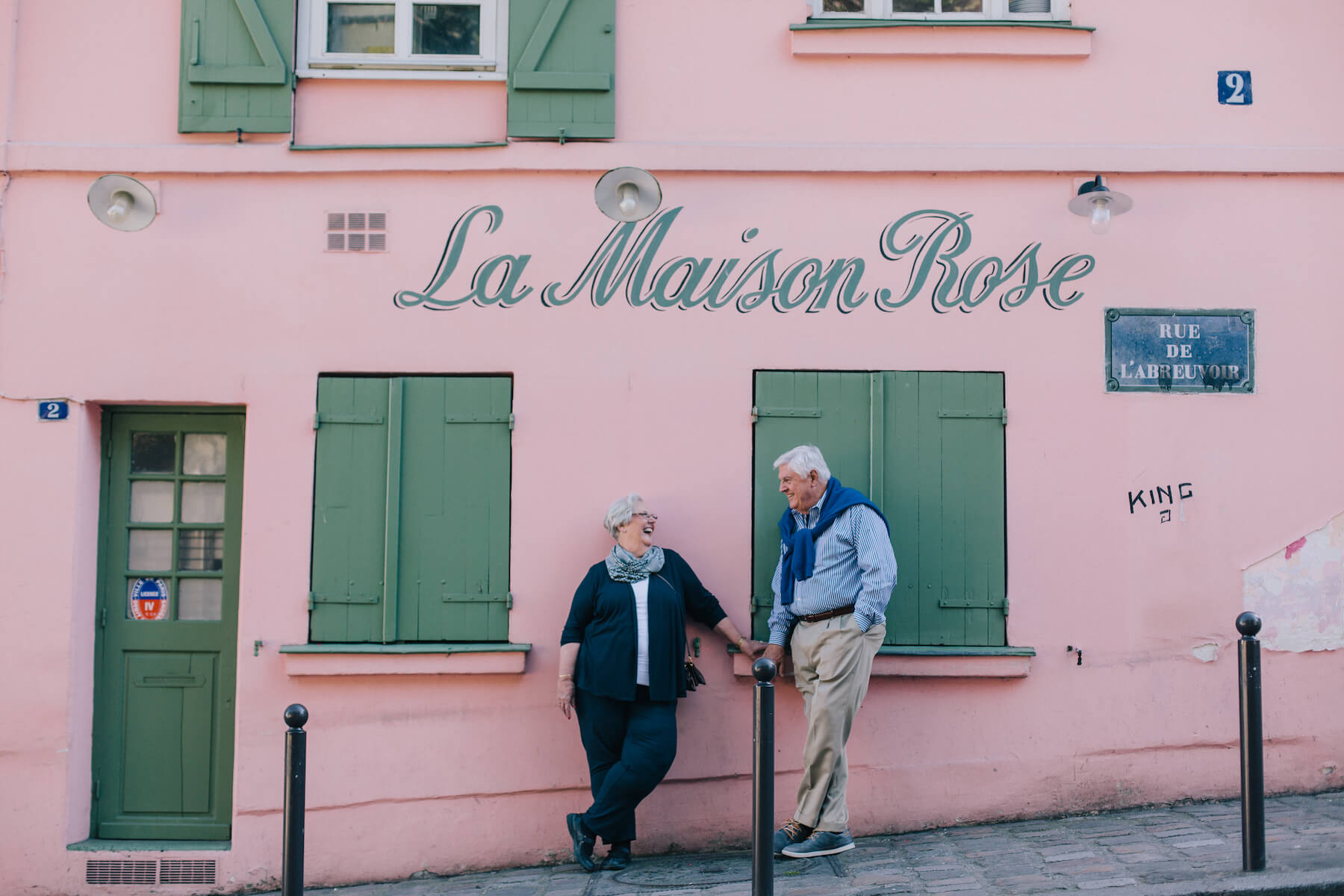 Mature couple laughing together in front of pink feature wall at La Maison Rose in Paris, France