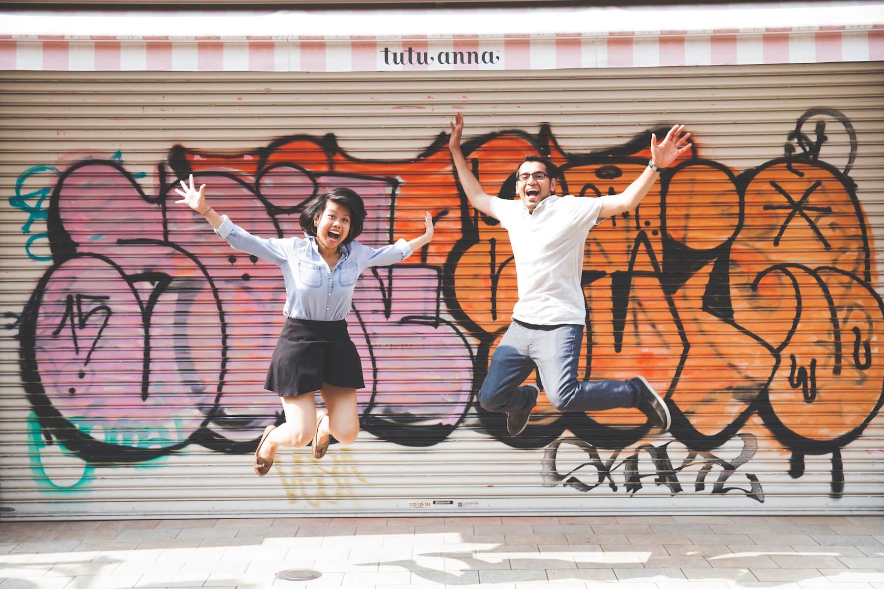 Couple jumping up in the air smiling in front of a graffiti wall in Tokyo, Japan