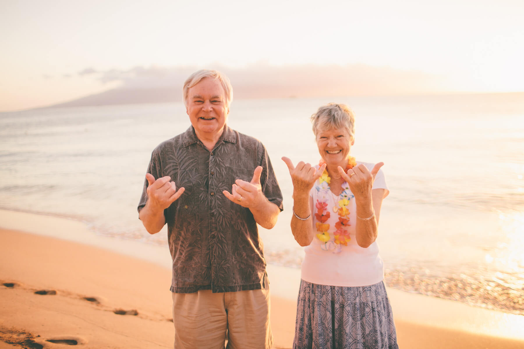 Mature couple smiling and giving the "Aloha" hand sign with both hands in Maui, Hawaii USA