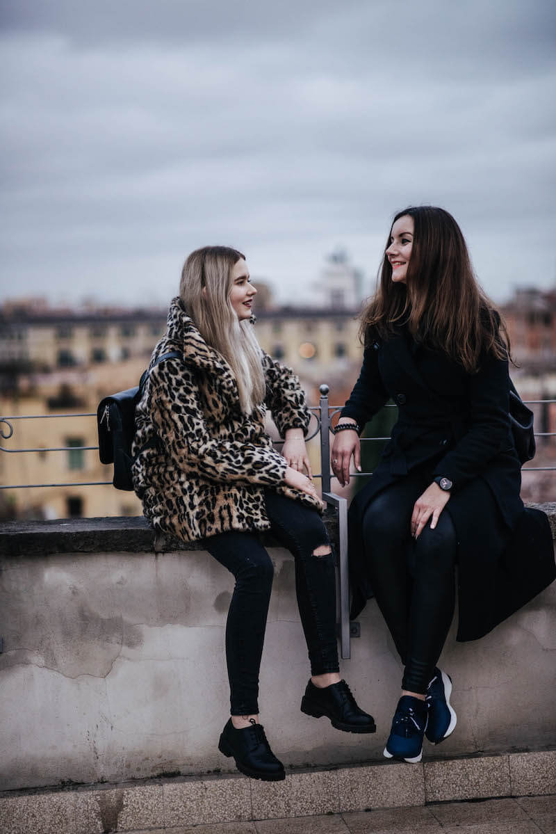 Sisters sitting on wall ledge smiling on a family trip in Rome, Italy