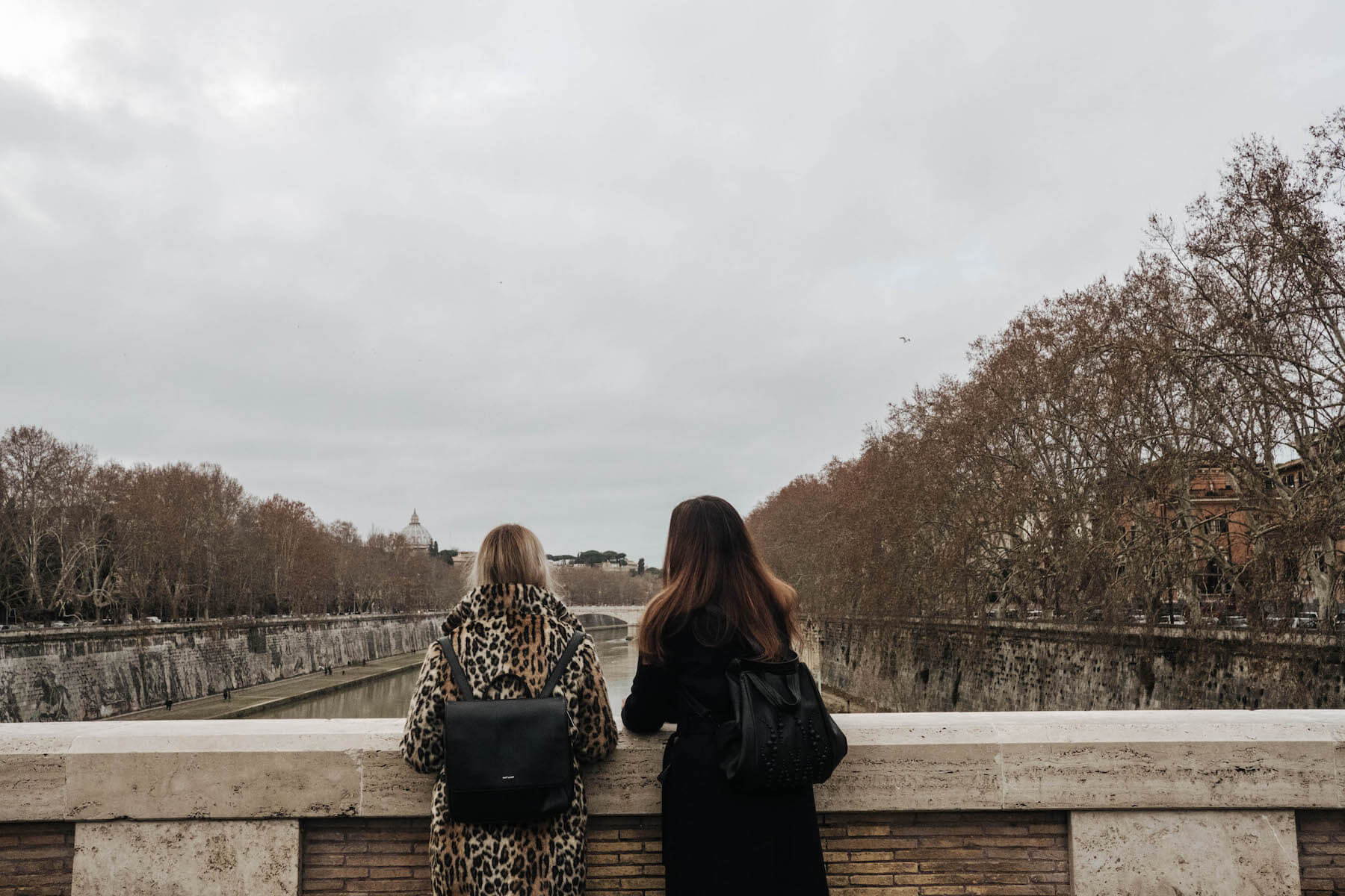 Sisters on a bridge looking out over a river on a family trip in Rome, Italy