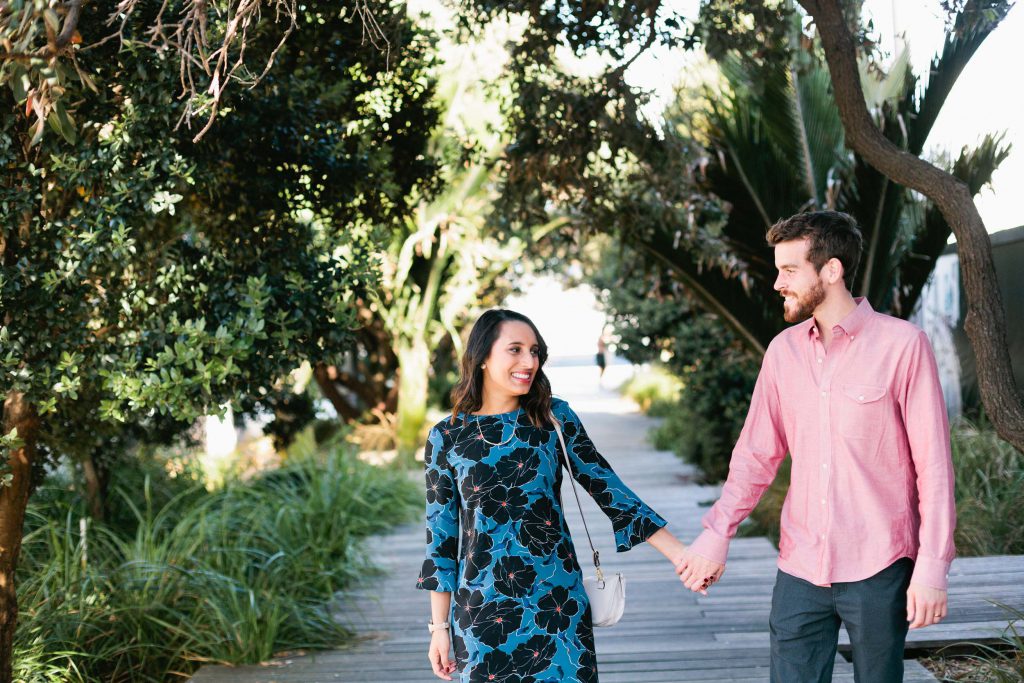 A couple walks hand in hand down a street lined with trees in Auckland