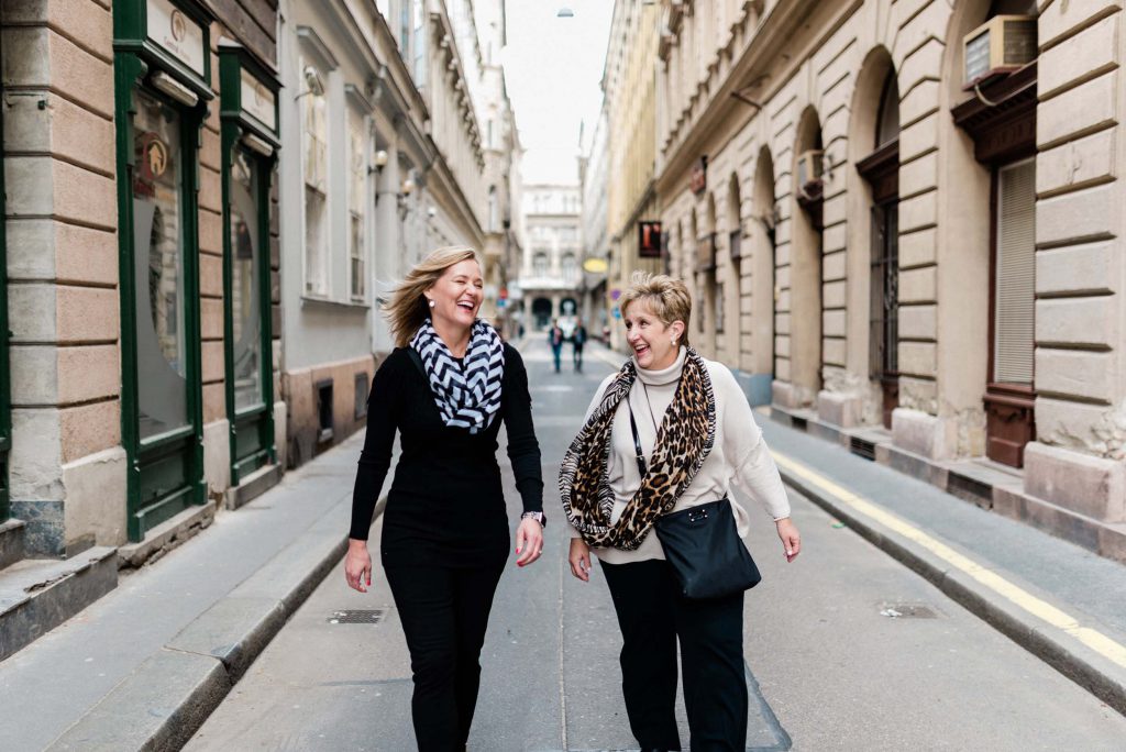Two women walk down the street laughing in Budapest.