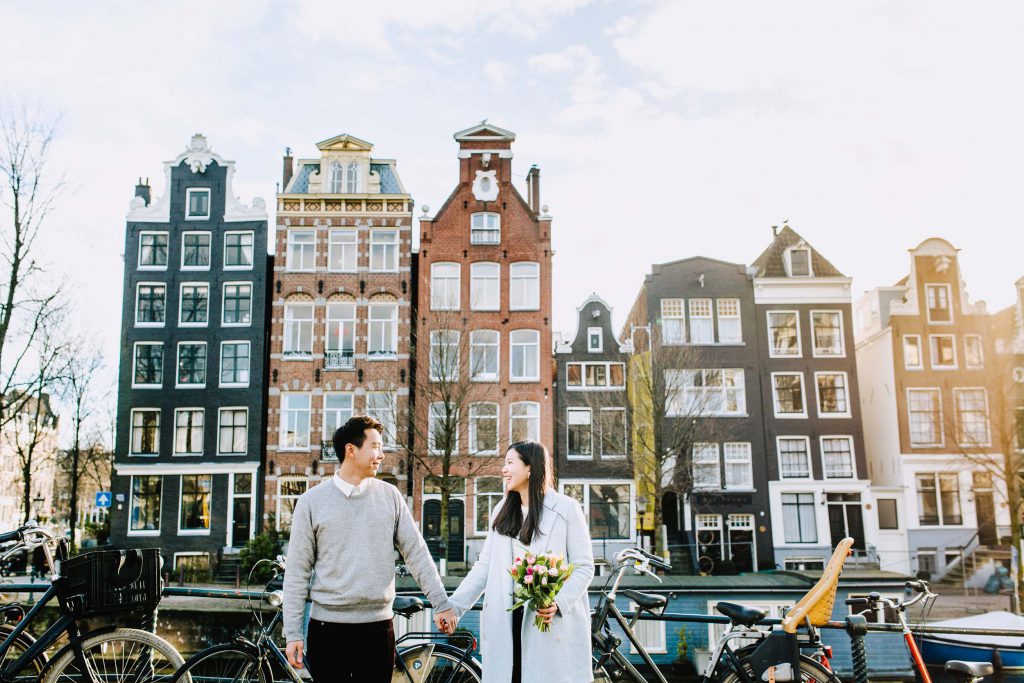 A couple holds hands while the woman holds a bouquet of tulips in Amsterdam.