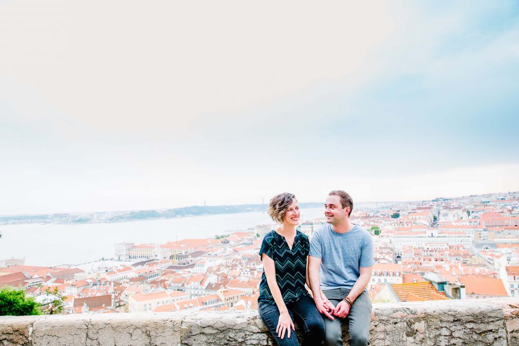 A couple sits on a ledge overlooking a view of Lisbon.