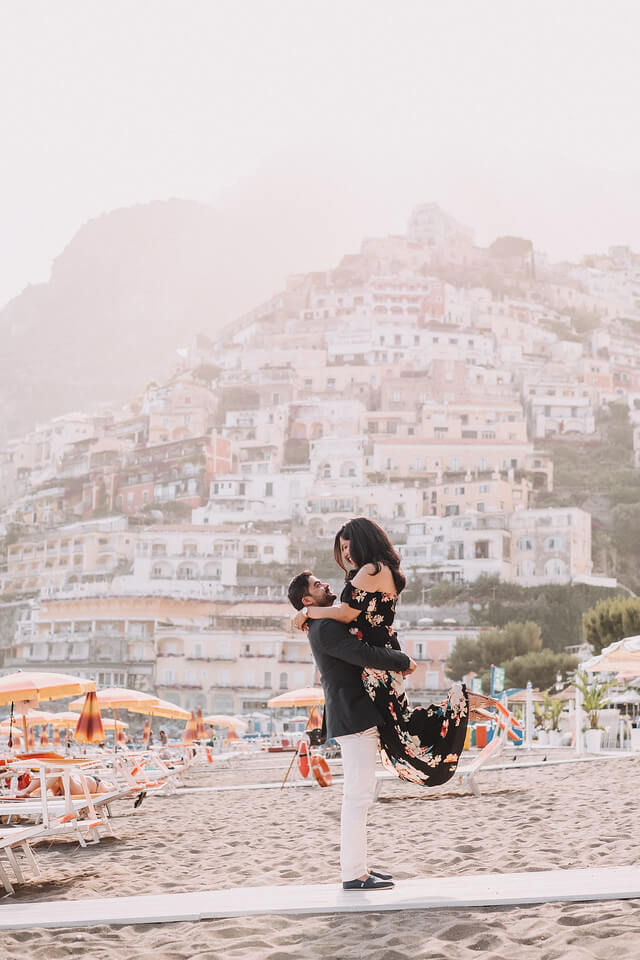 Man holding up his female partner on a beach in Amalfi Coast, Italy on a couples trip