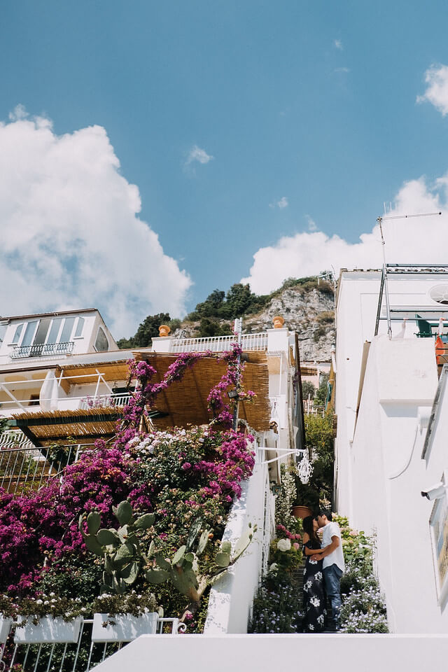 Couple kissing while they hide between two buildings covered in flowers for privacy in Amalfi Coast, Italy