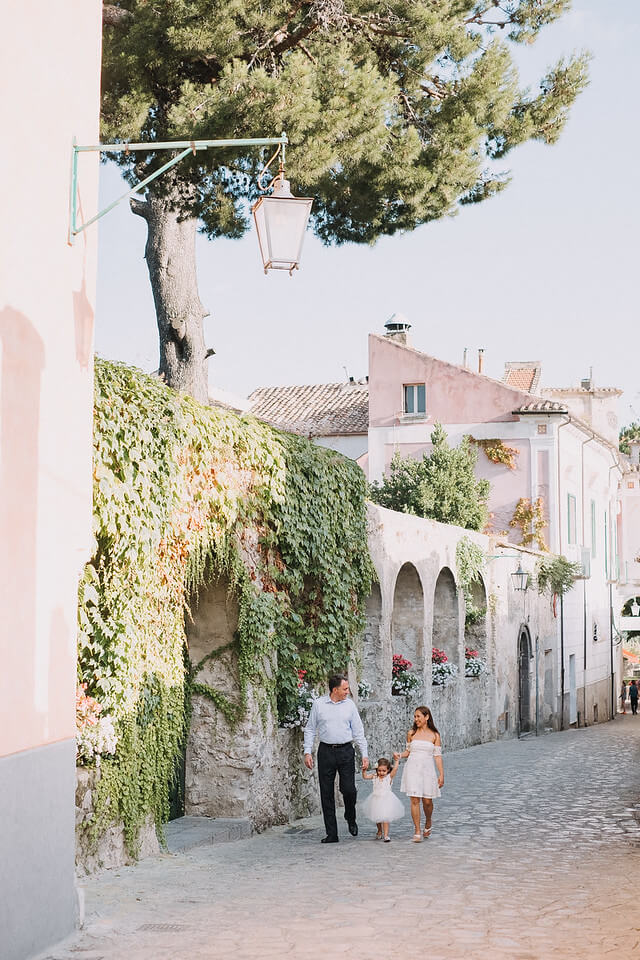 Family of three with an infant daughter walking along a cobblestone pathway in Amalfi Coast, Italy