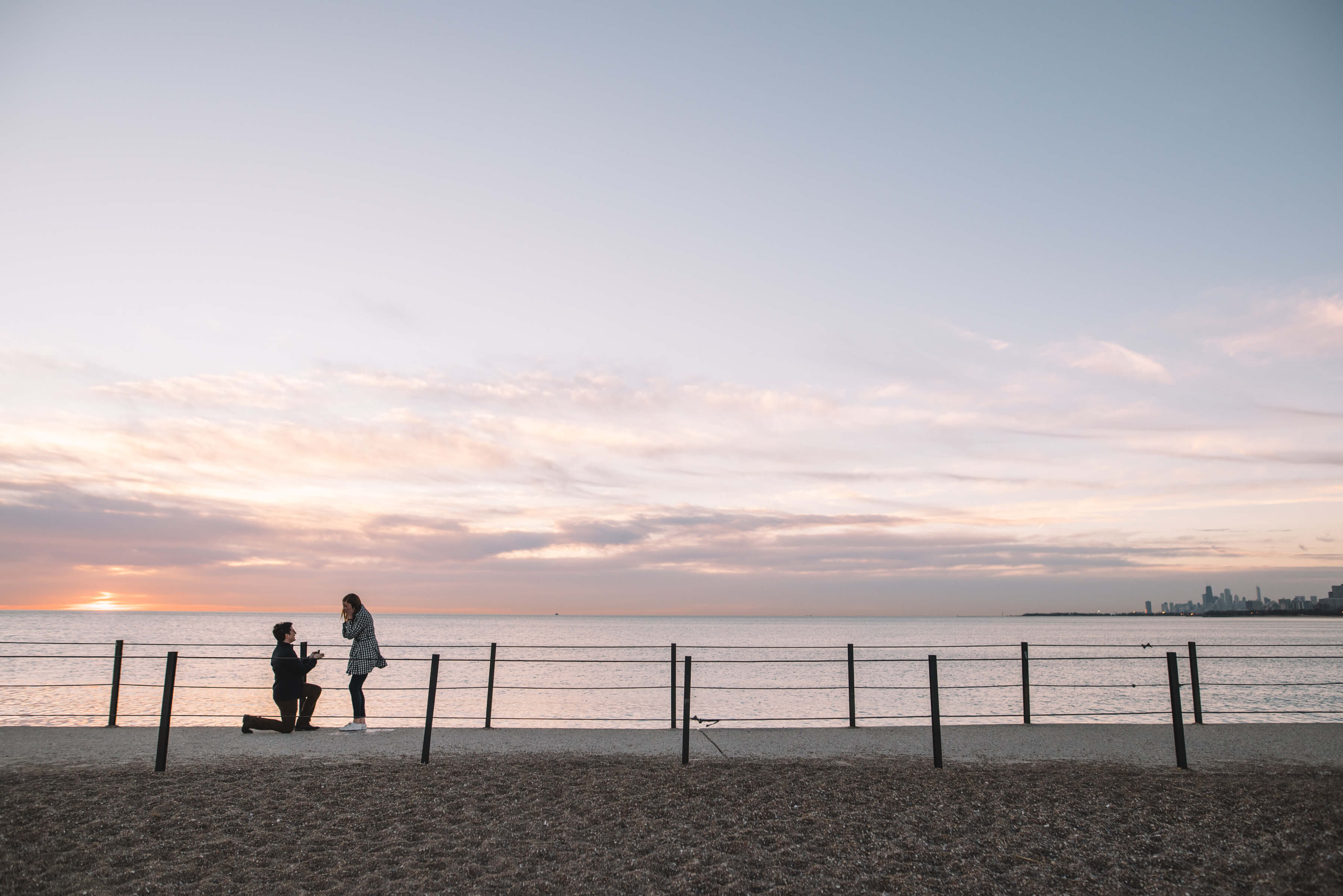 Man proposing to his partner at sunset with the ocean and downtown Chicago in the background