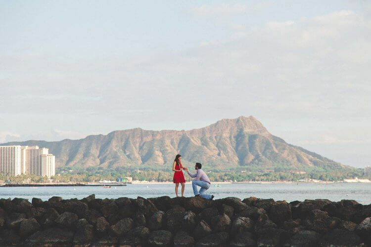 Woman shocked and happy at her partner's surprise proposal at Waikiki Beach Rock Wall in Honolulu, Hawaii USA