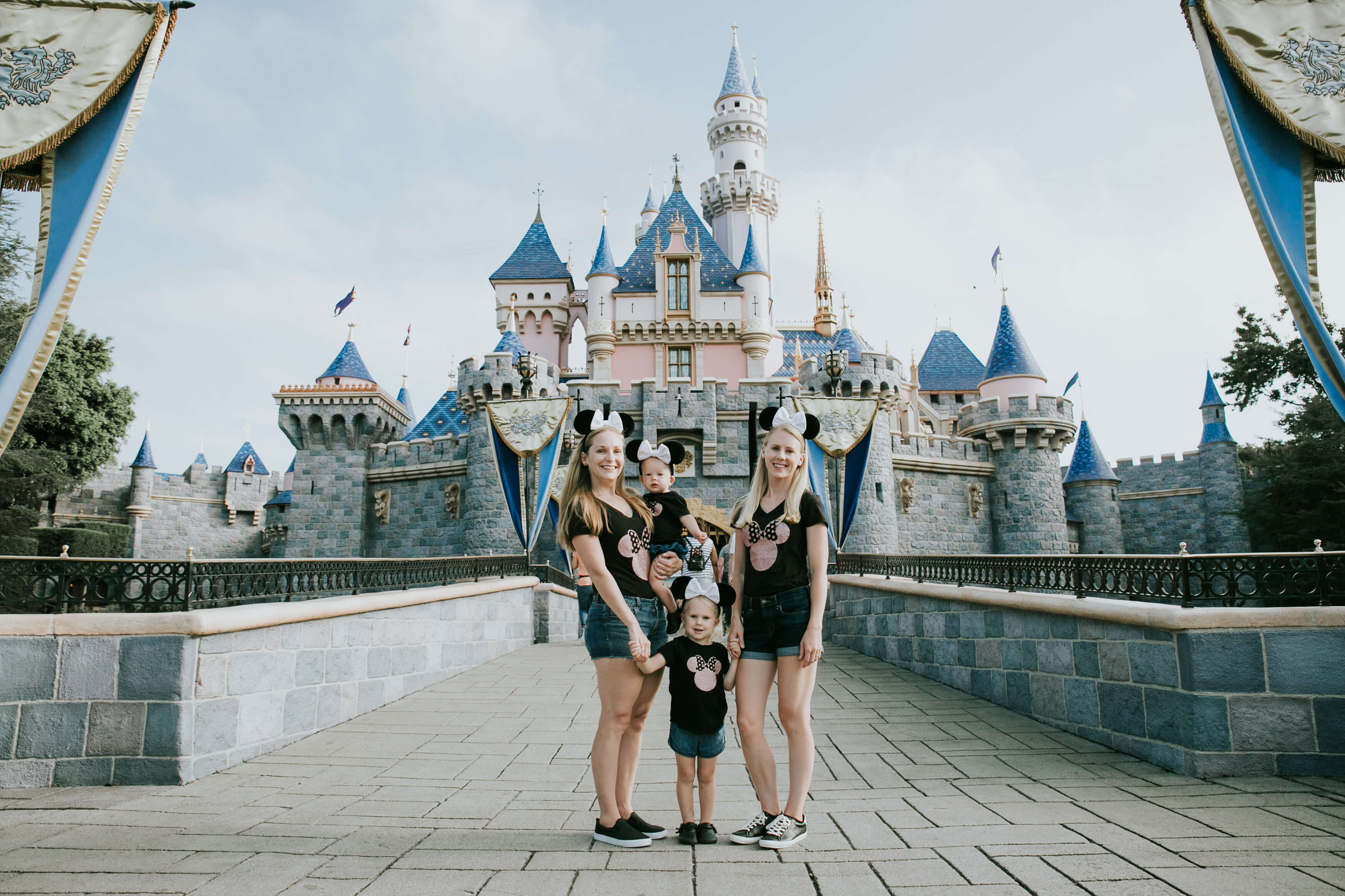 LGBTQ+ family with two young kids standing in front of the castle in Disneyland, Anaheim