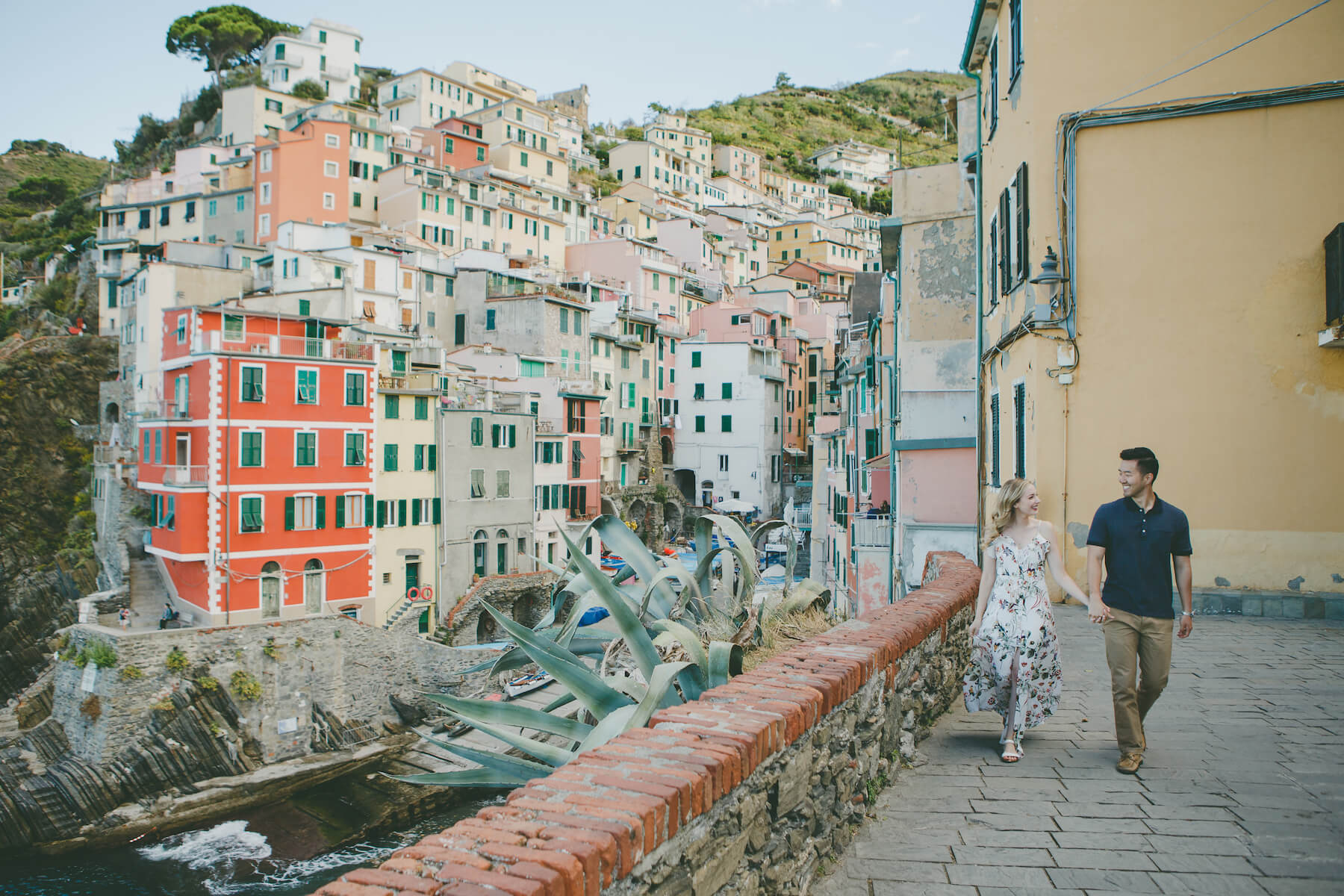 a couple walking and holding hands, with the background being colourful cliffside houses in Cinque Terre, Italy