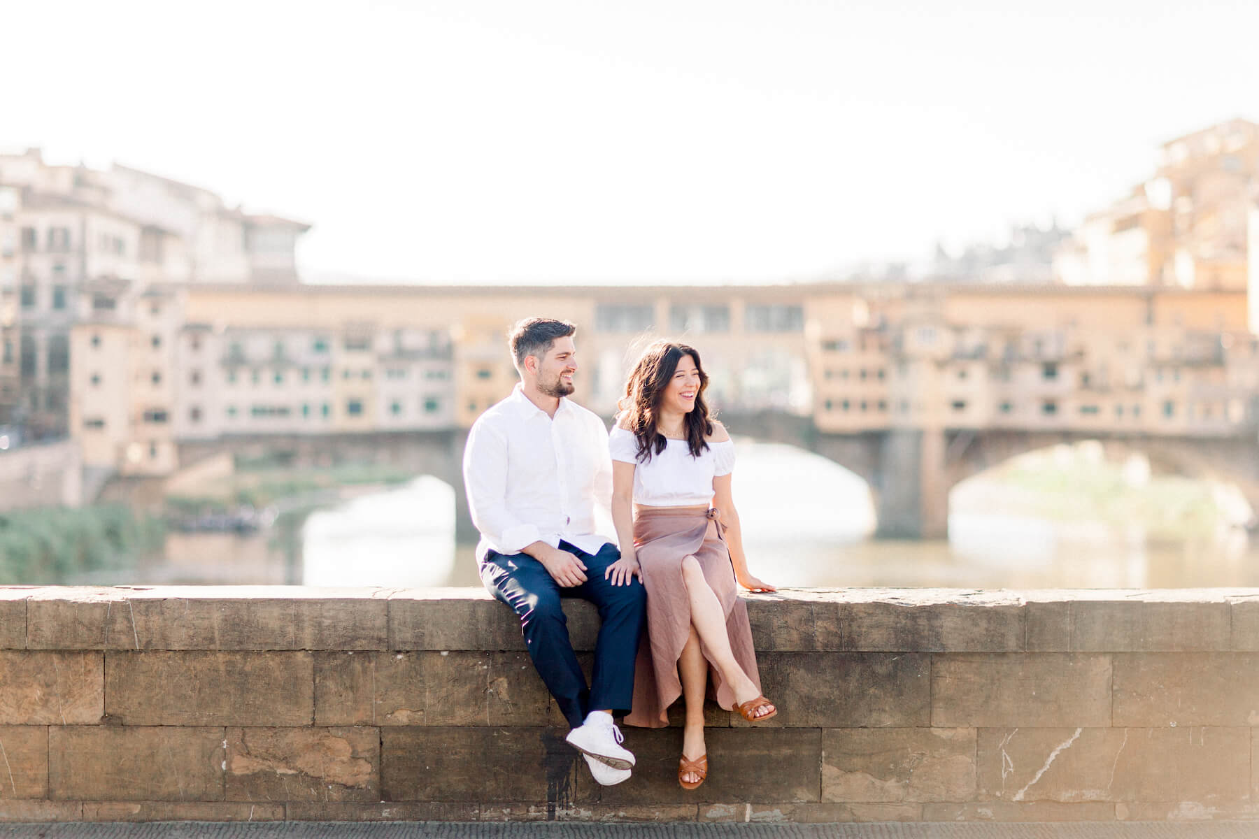 couple sitting down on the bridge overlooking ponte vecchio in Florence, Italy
