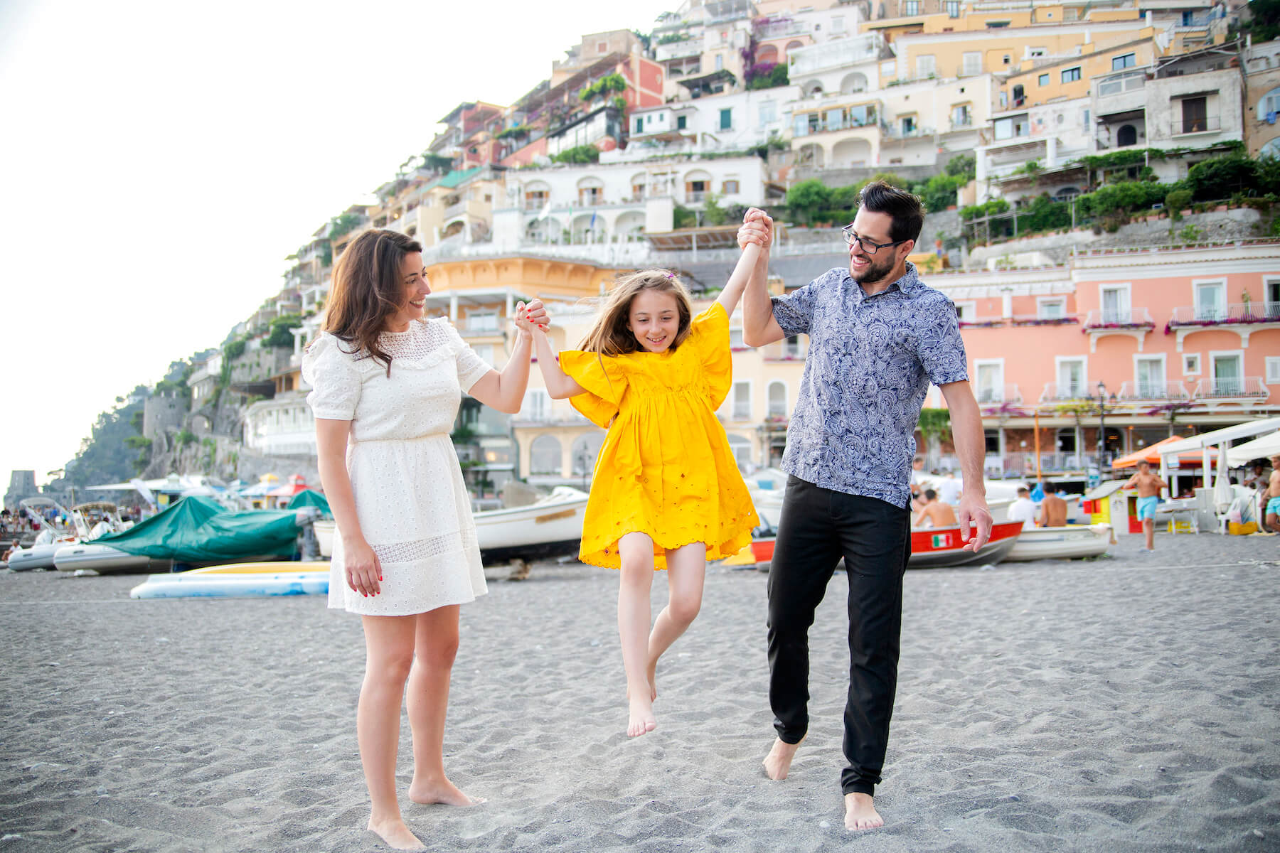 a family with a young girl, the parents are lifting her and having fun on the beach in Positano, Italy