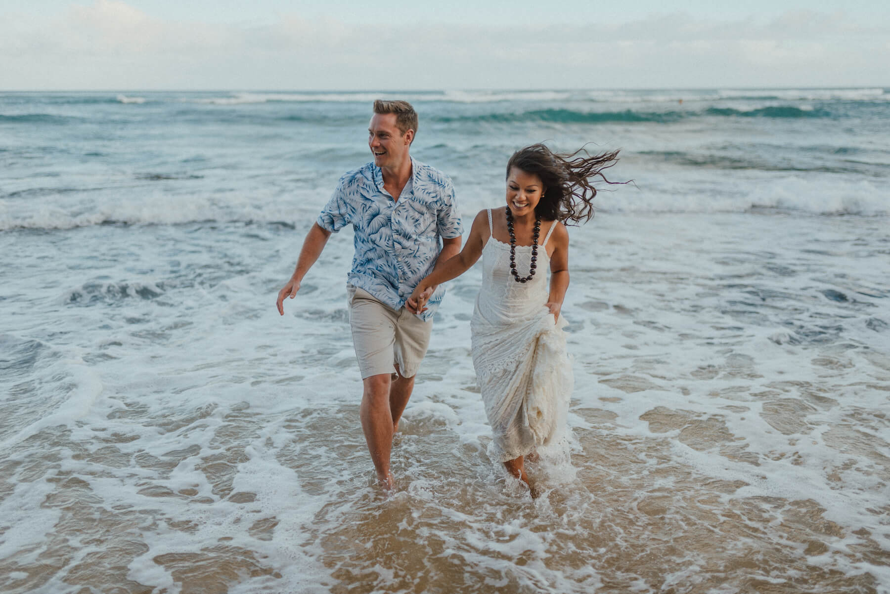 A couple on a couple's trip running in the water, holding hands in Honolulu, Hawaii