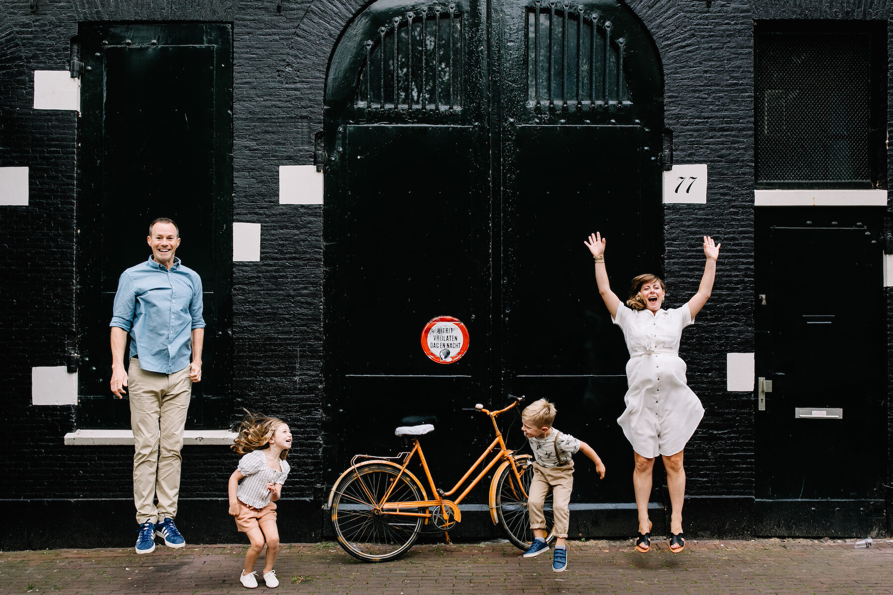 a family jumping and laughing in front of black brick building in Amsterdam, Netherlands