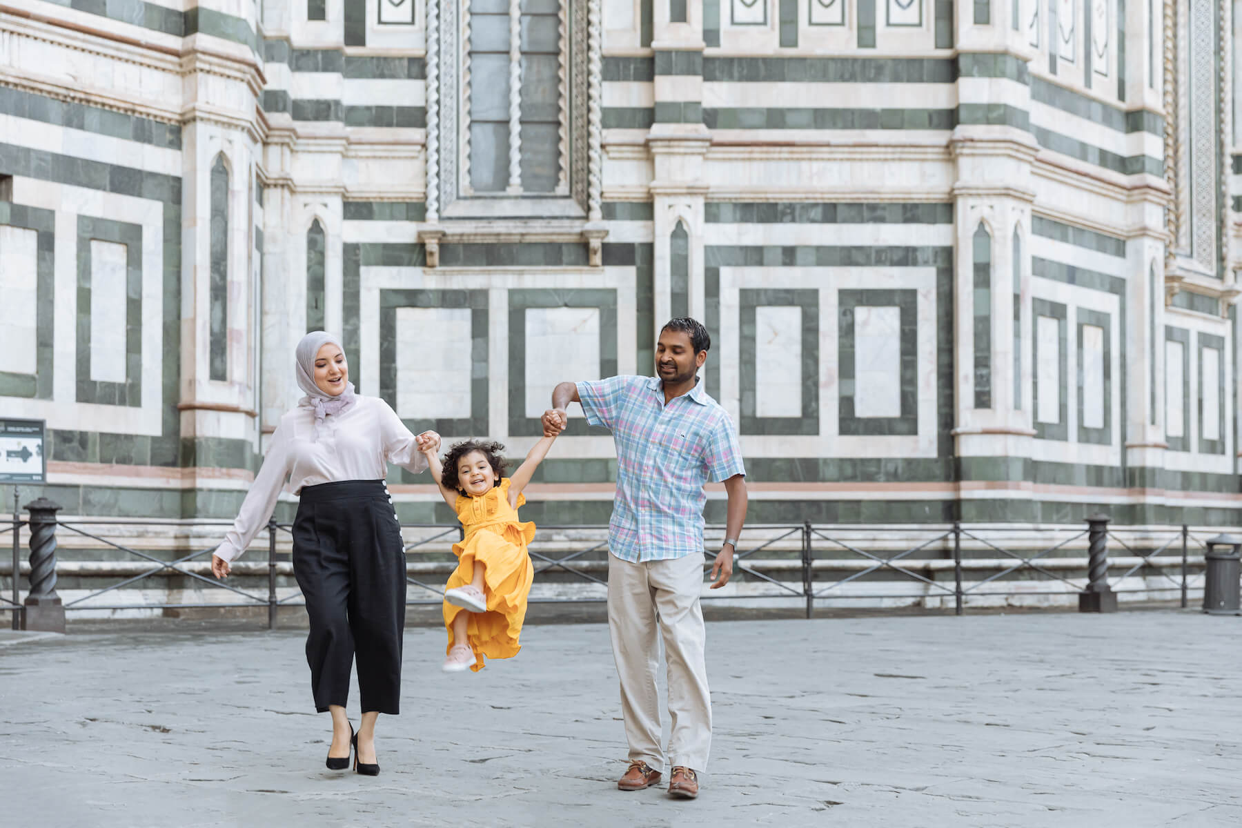 family with a little girl, swinging her and walking in Florence, Italy