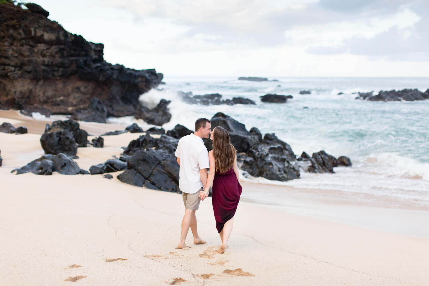 A couple holding hands and looking away from the camera, walking towards the ocean in Honolulu, Hawaii