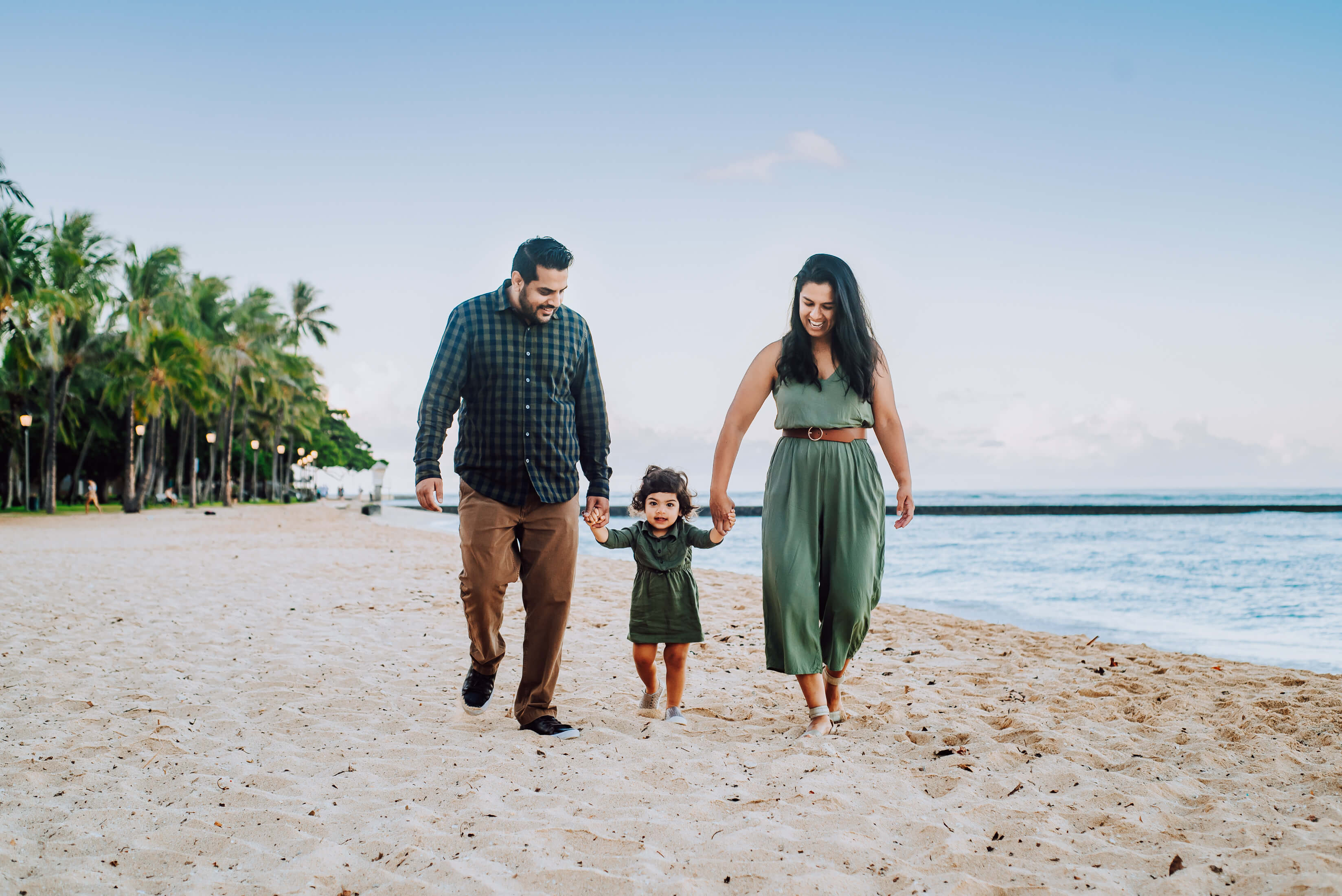 A family holding hands, laughing and walking on the beach in Honolulu, Hawaii