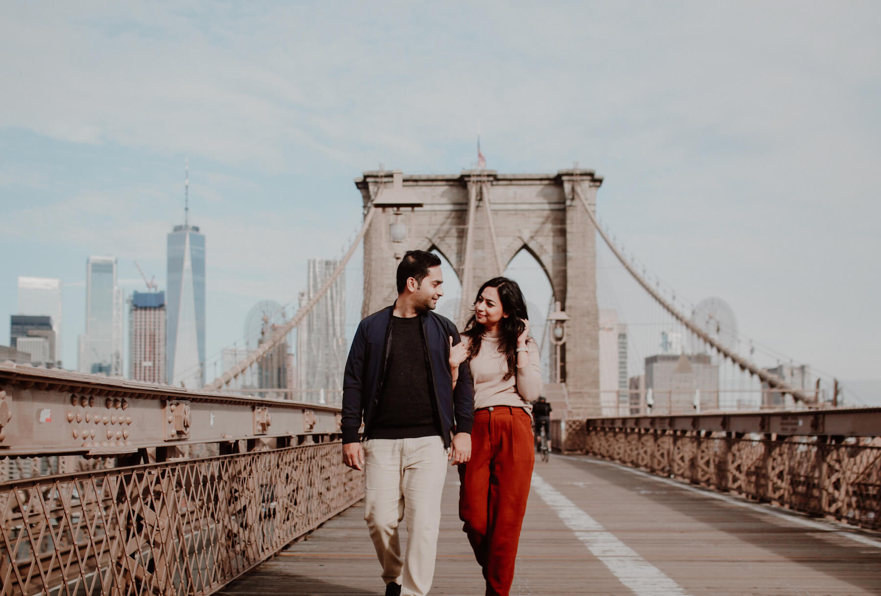 Couple looking at each other, holding hands walking on Brooklyn Bridge, New York City, New York