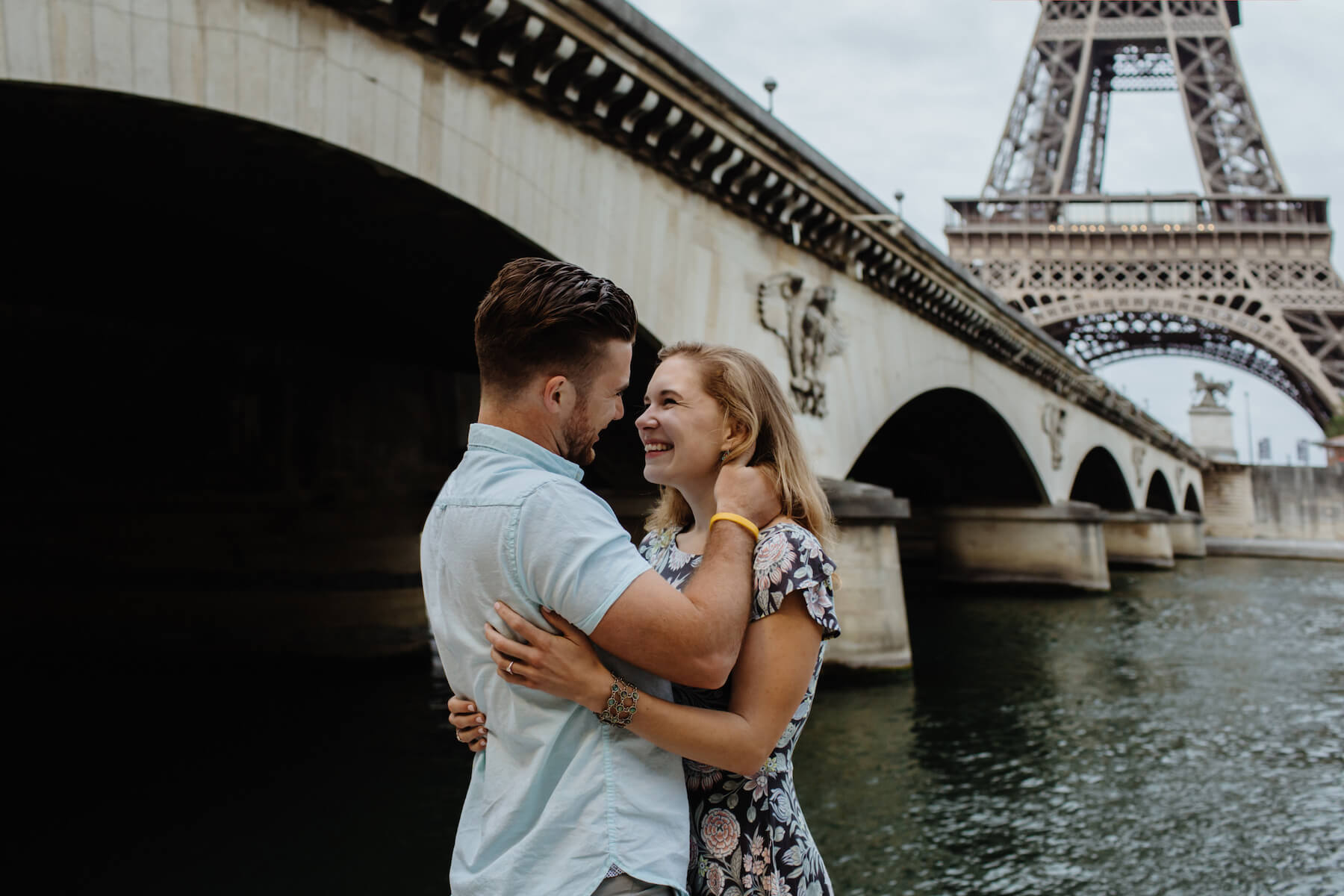 Couple under a bridge and near the Eiffel Tower, holding each other and smiling in Paris, France