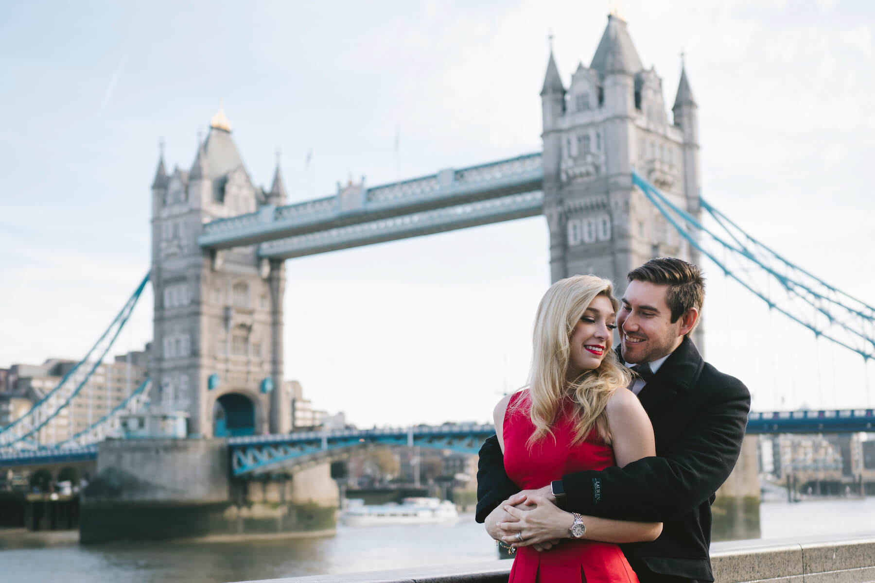 couple sitting and holding each other, dressed up in formal attire in front of the Tower Bridge in London, England