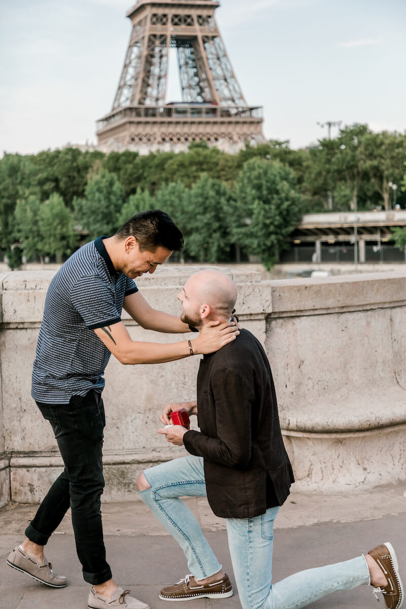 A man holding another man and saying yes to the wedding proposal in front of the Eiffel tower in Paris, France