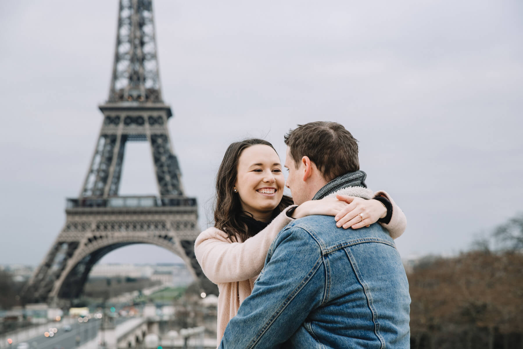 A woman holding a man, smiling in front of the Eiffel tower in Paris, France