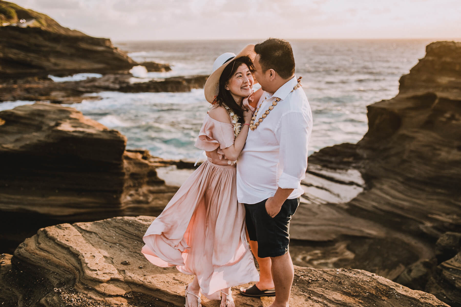 A couple hugging each other, she is holding onto her hat in Honolulu, Hawaii