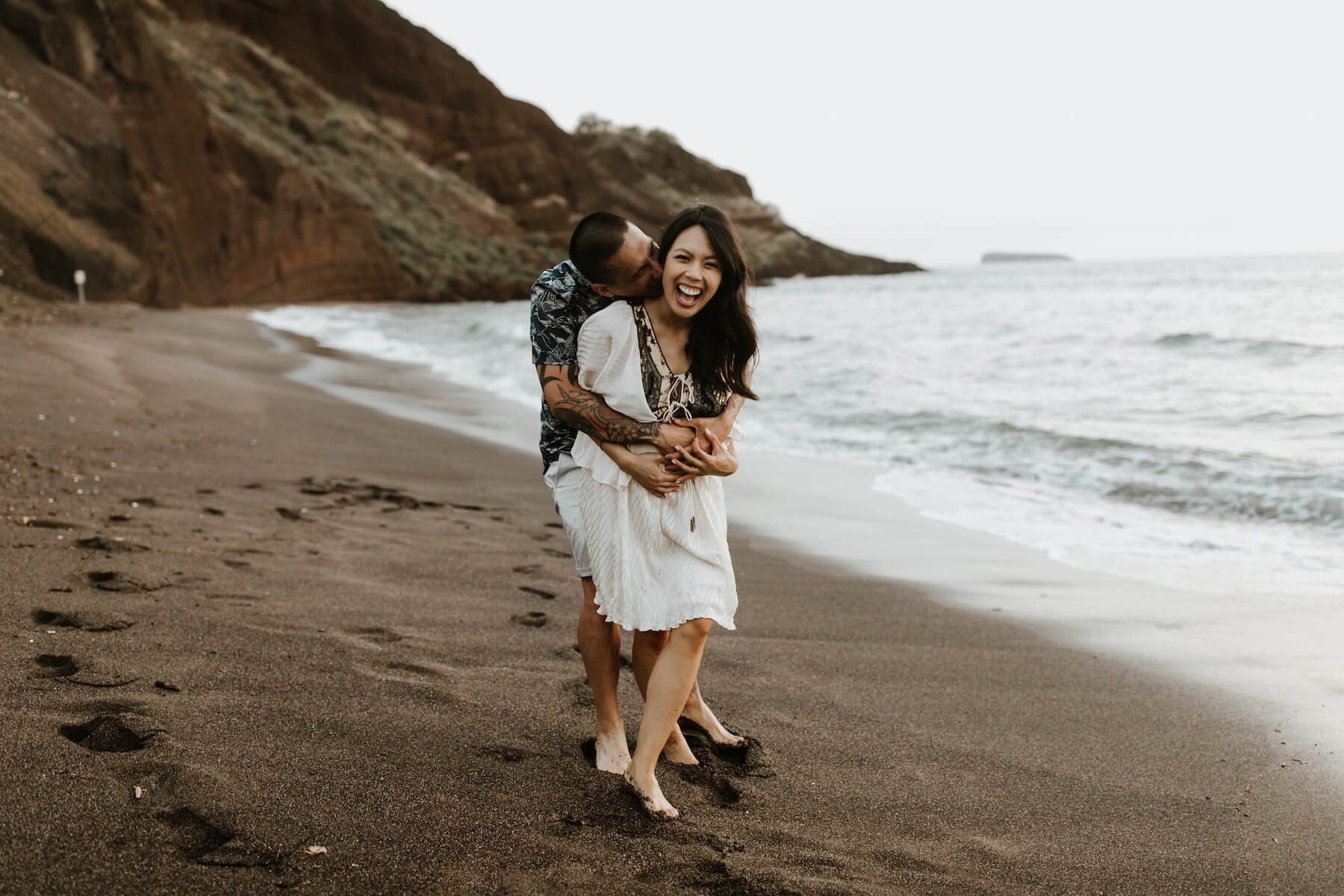 pregnant couple holding each other laughing on the beach in Maui, Hawaii