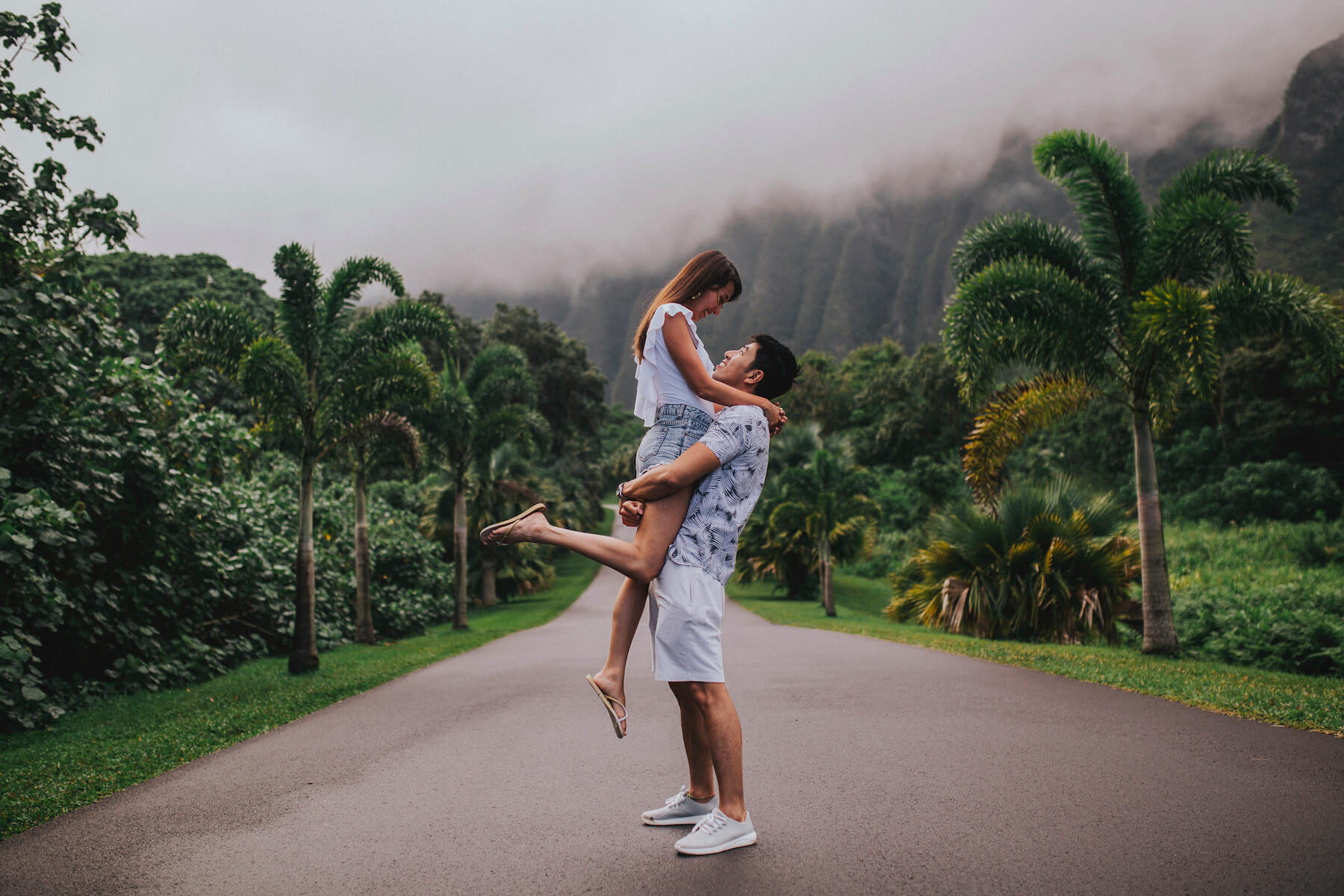 A couple standing in the middle of the road, she is being lifted and they're looking at each other in Honolulu, Hawaii