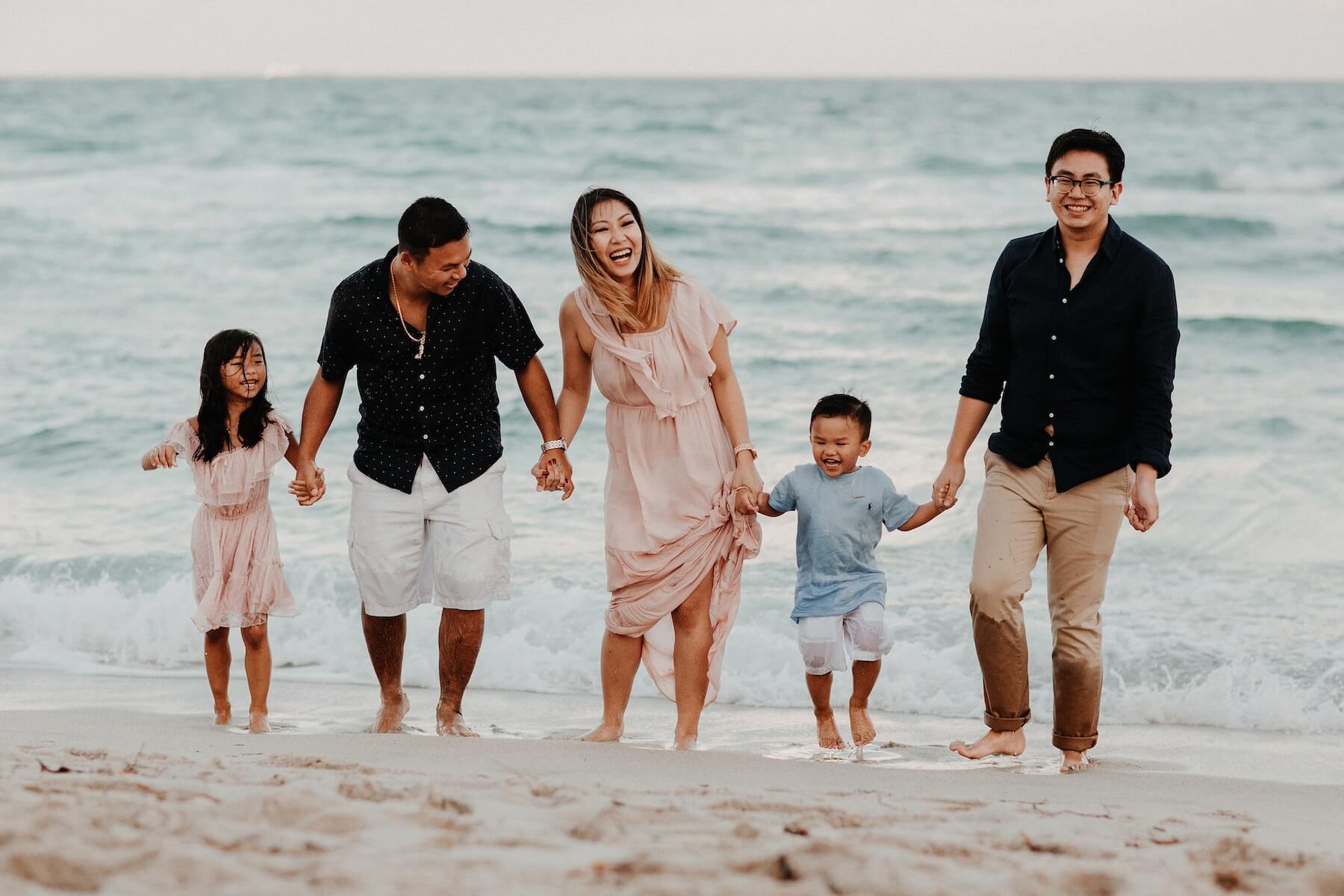 a family holding hands on the beach, running away from the ocean in Miami, Florida