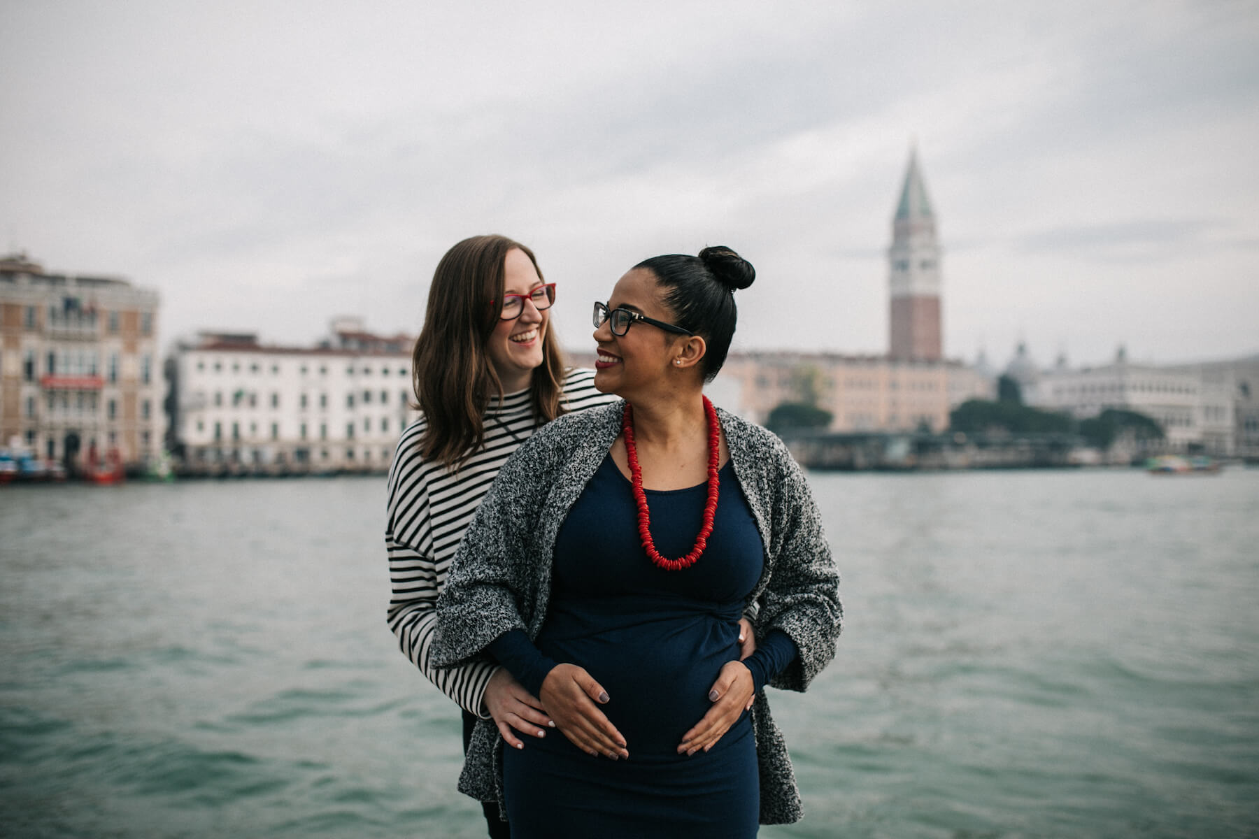 couple expecting a baby, on a babymoon trip and near the canal with arms around each other in Venice, Italy